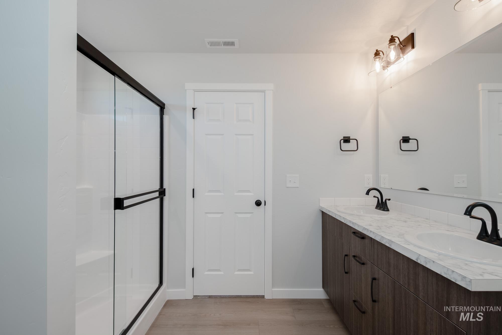 Full bathroom featuring double vanity, a stall shower, and light wood-style floors