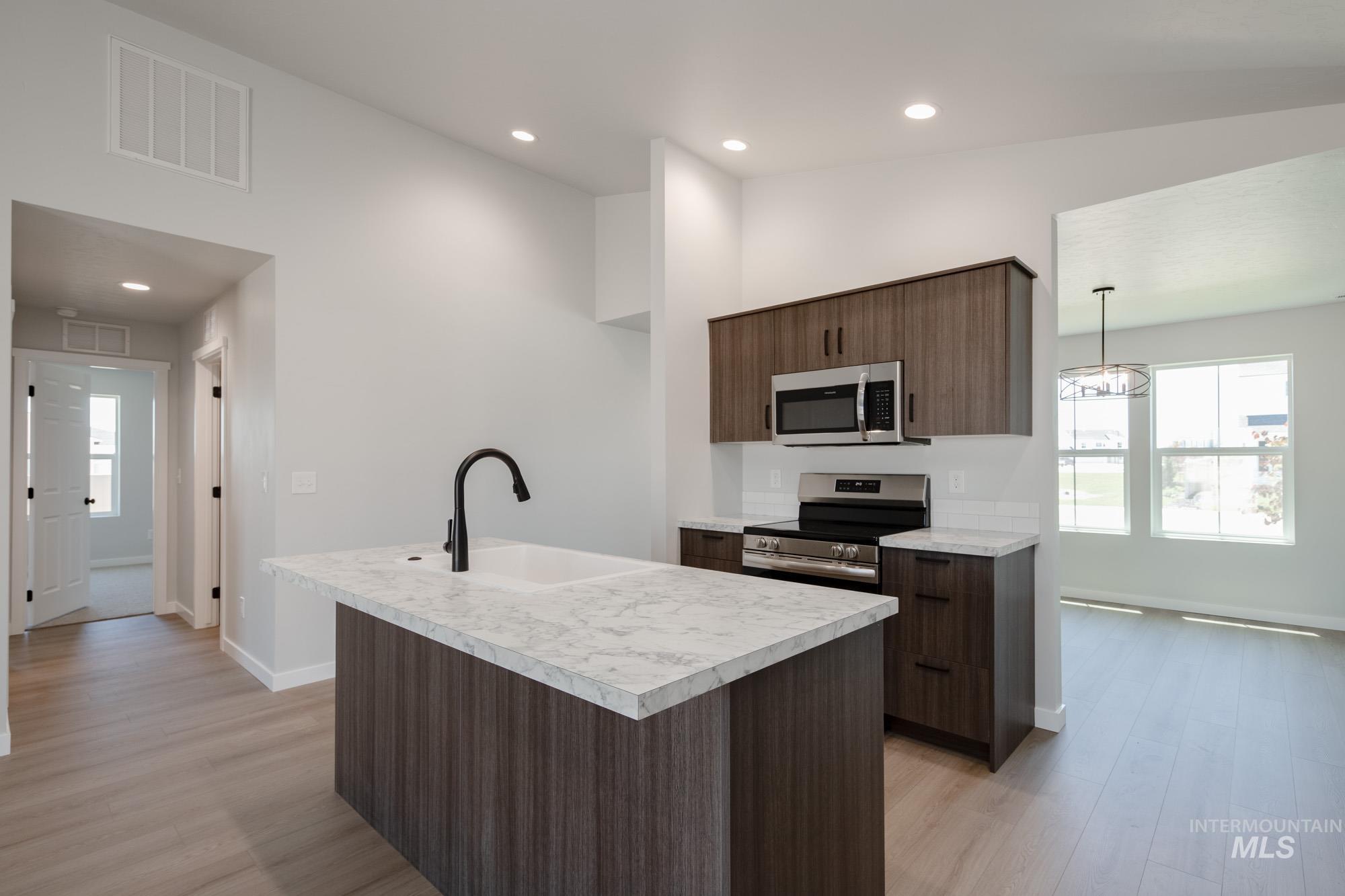 Kitchen featuring light countertops, appliances with stainless steel finishes, recessed lighting, light wood-style flooring, and a center island with sink