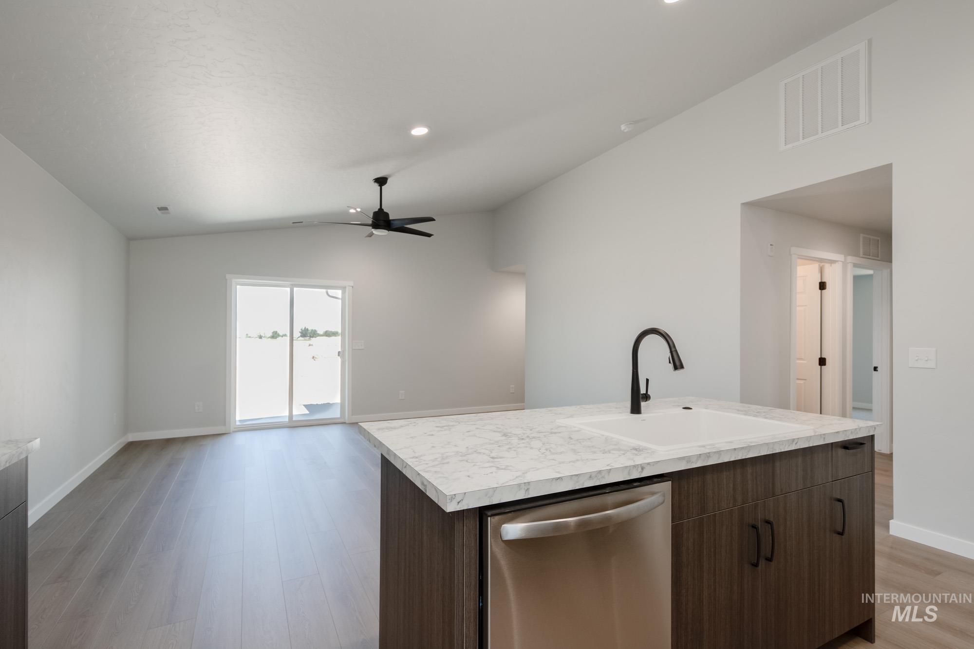 Kitchen featuring stainless steel dishwasher, dark brown cabinetry, light countertops, open floor plan, and lofted ceiling