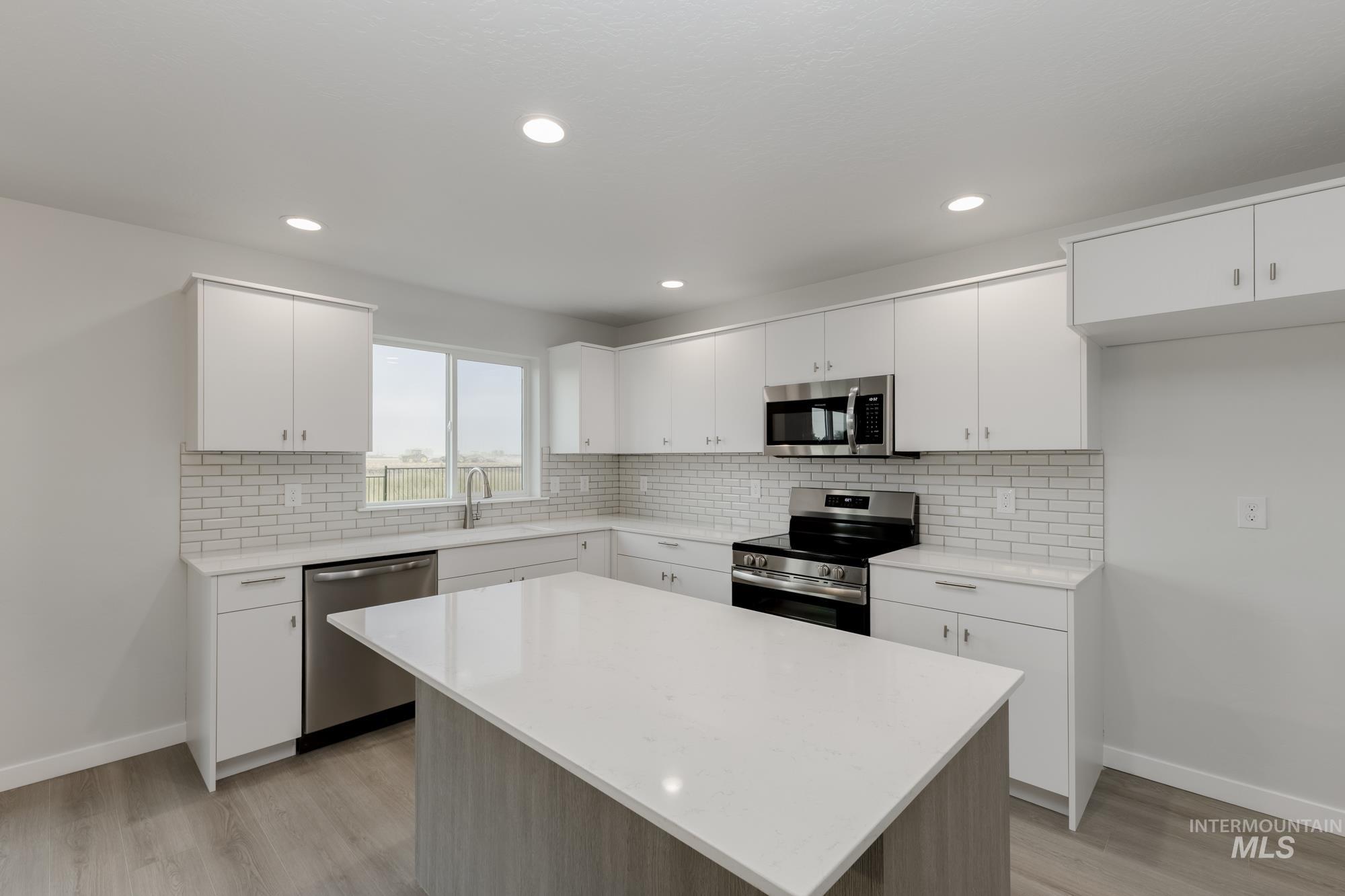 Kitchen featuring a kitchen island, appliances with stainless steel finishes, backsplash, white cabinets, and recessed lighting
