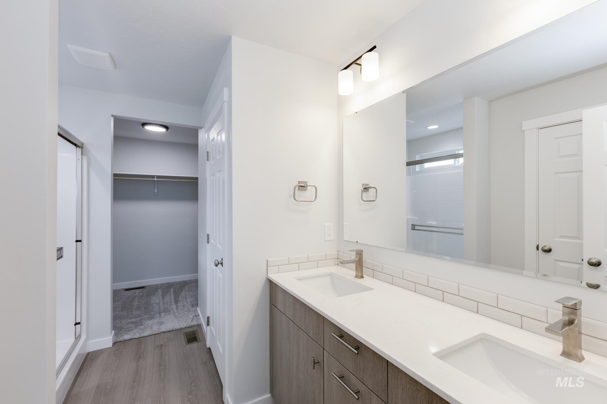 Bathroom featuring a walk in closet, light wood finished floors, double vanity, and a shower stall