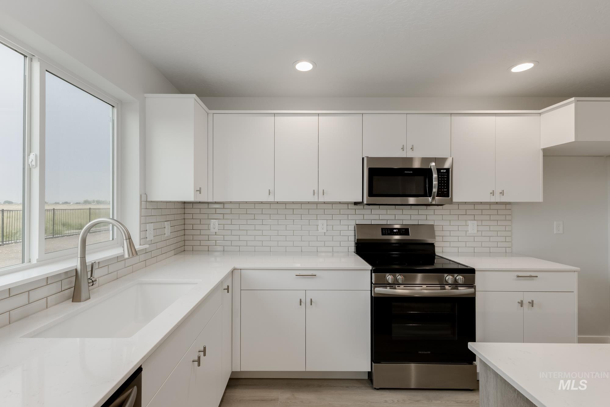 Kitchen featuring appliances with stainless steel finishes, white cabinets, decorative backsplash, light stone countertops, and recessed lighting