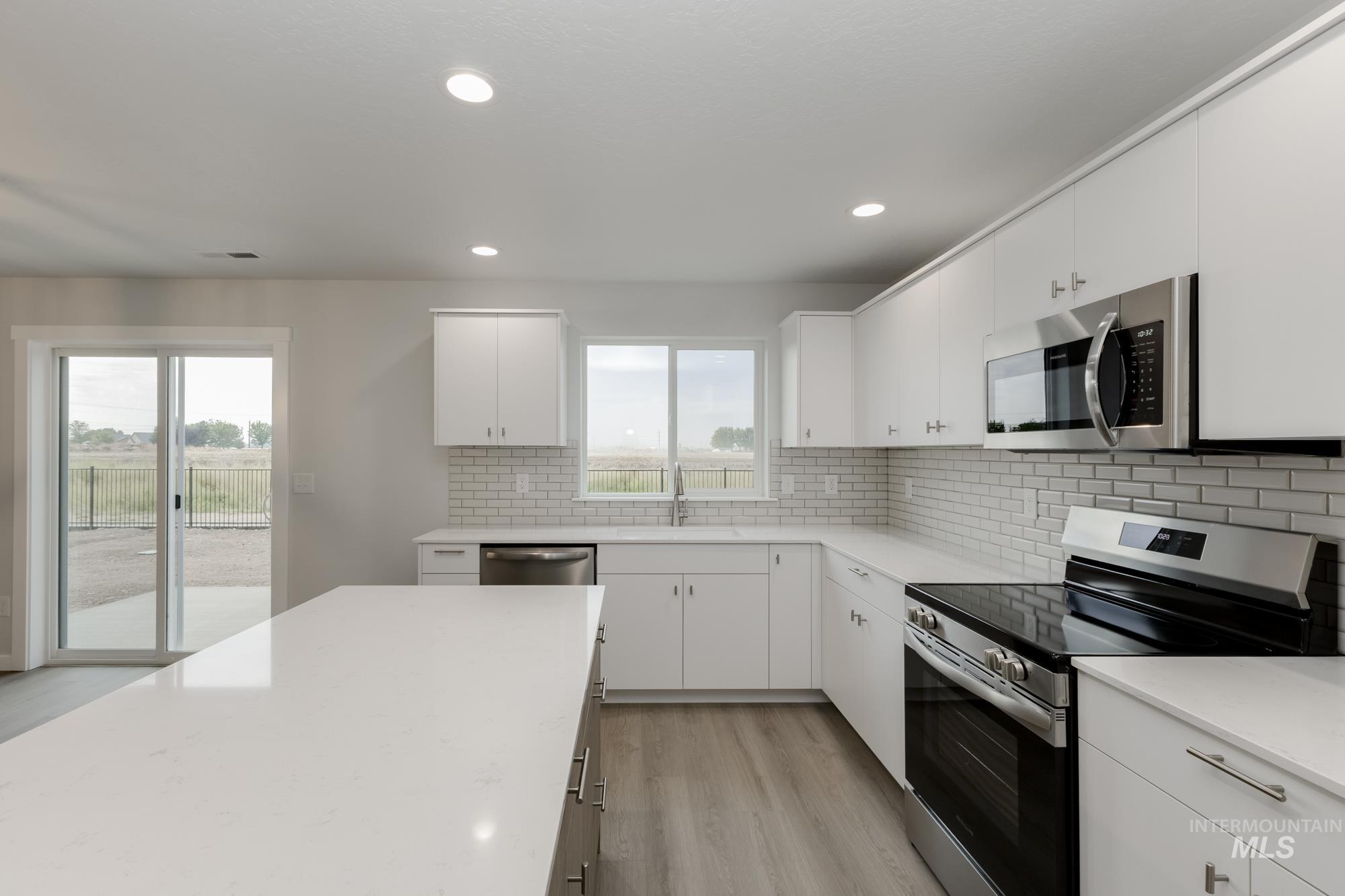 Kitchen featuring stainless steel appliances, decorative backsplash, white cabinets, light wood-type flooring, and recessed lighting