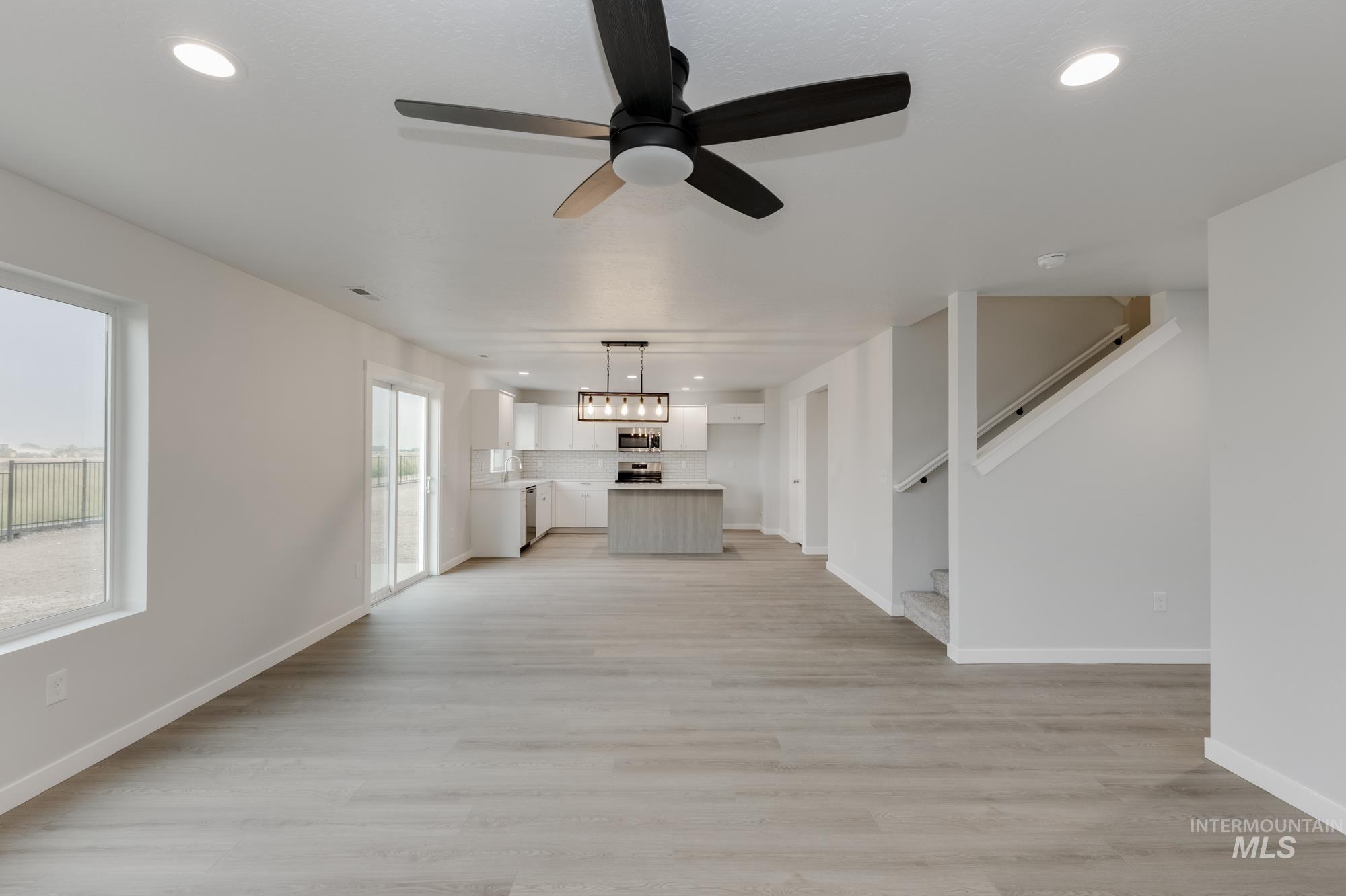 Unfurnished living room with recessed lighting, light wood-style flooring, ceiling fan, and stairway