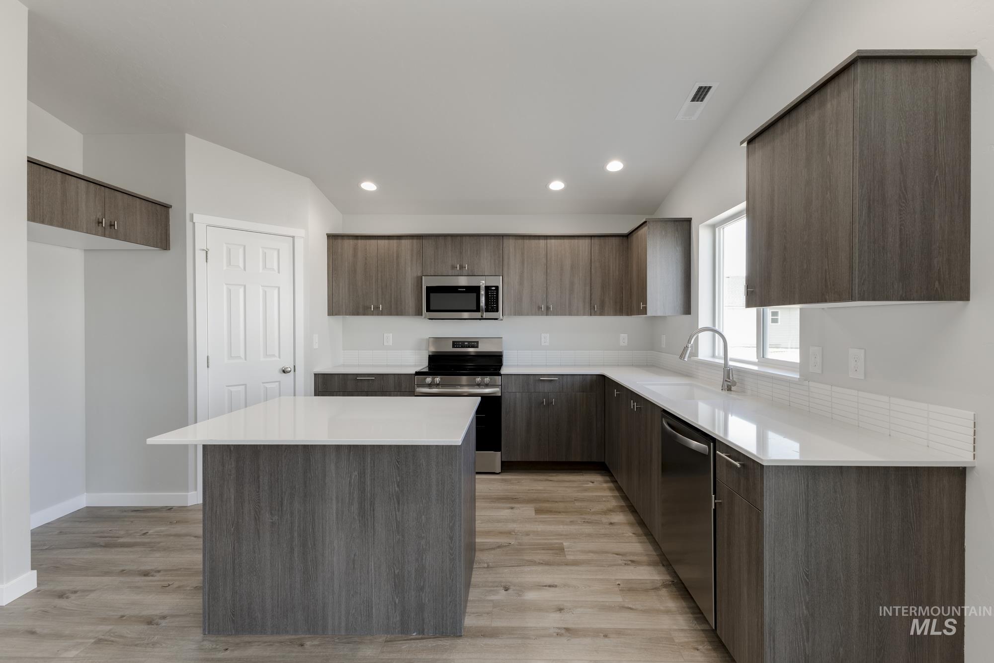Kitchen featuring modern cabinets, stainless steel appliances, a kitchen island, light wood-style floors, and recessed lighting