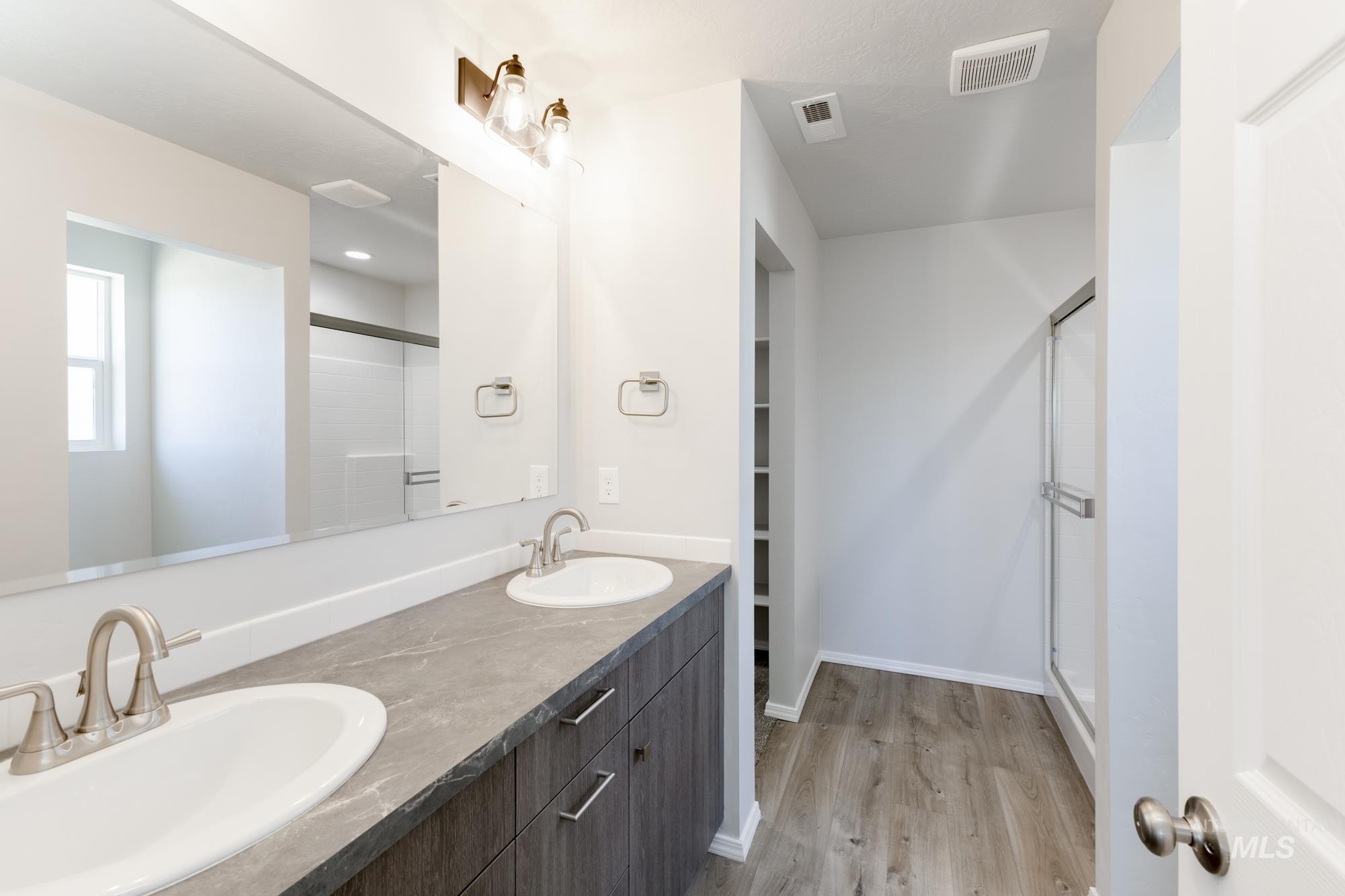 Bathroom featuring a stall shower, light wood-style floors, double vanity, and a walk in closet