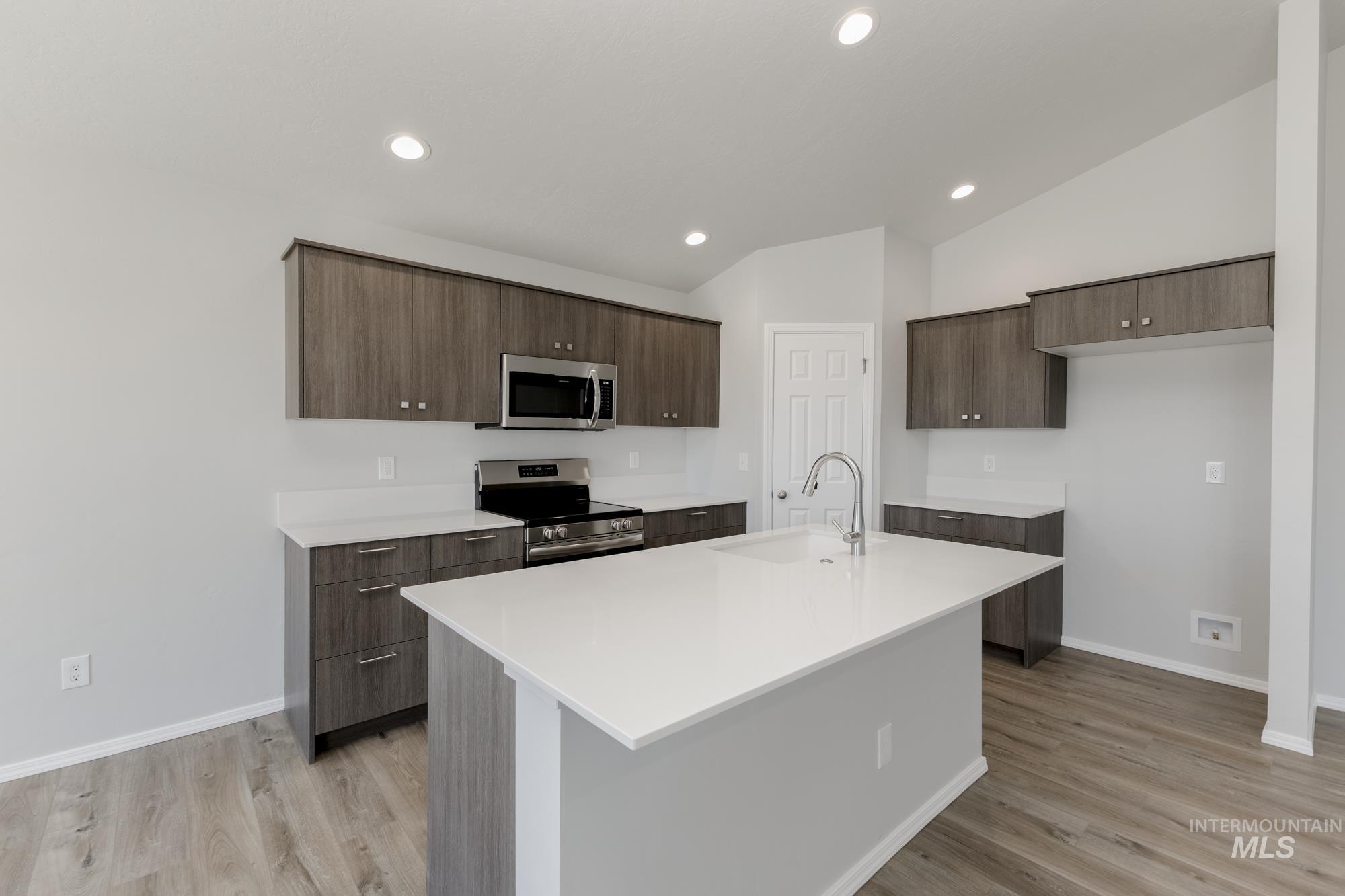 Kitchen featuring stainless steel appliances, modern cabinets, dark brown cabinetry, a kitchen island with sink, and light wood-style floors