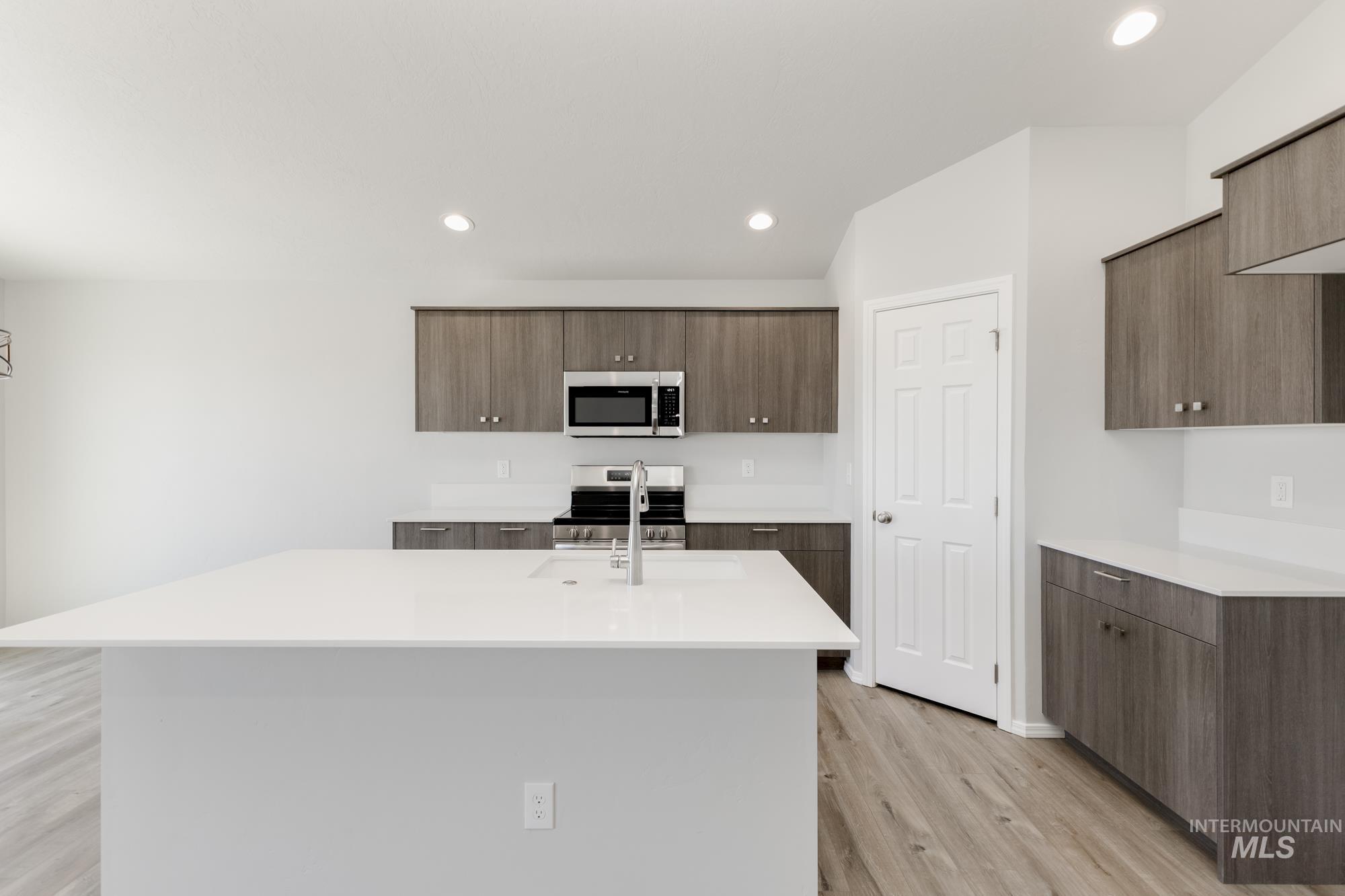 Kitchen with appliances with stainless steel finishes, light wood finished floors, modern cabinets, recessed lighting, and an island with sink