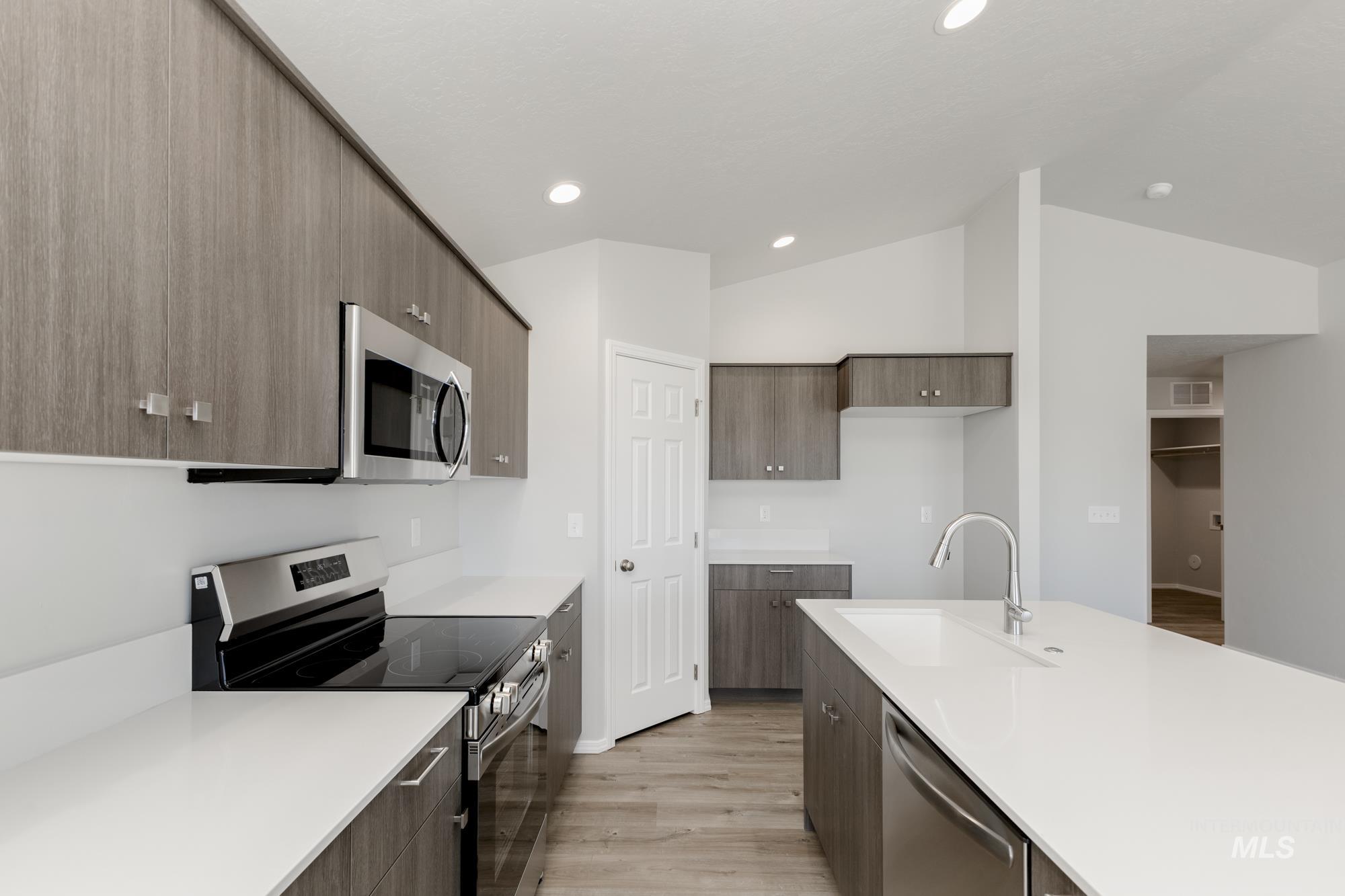 Kitchen with stainless steel appliances, modern cabinets, light wood-style flooring, vaulted ceiling, and light stone countertops