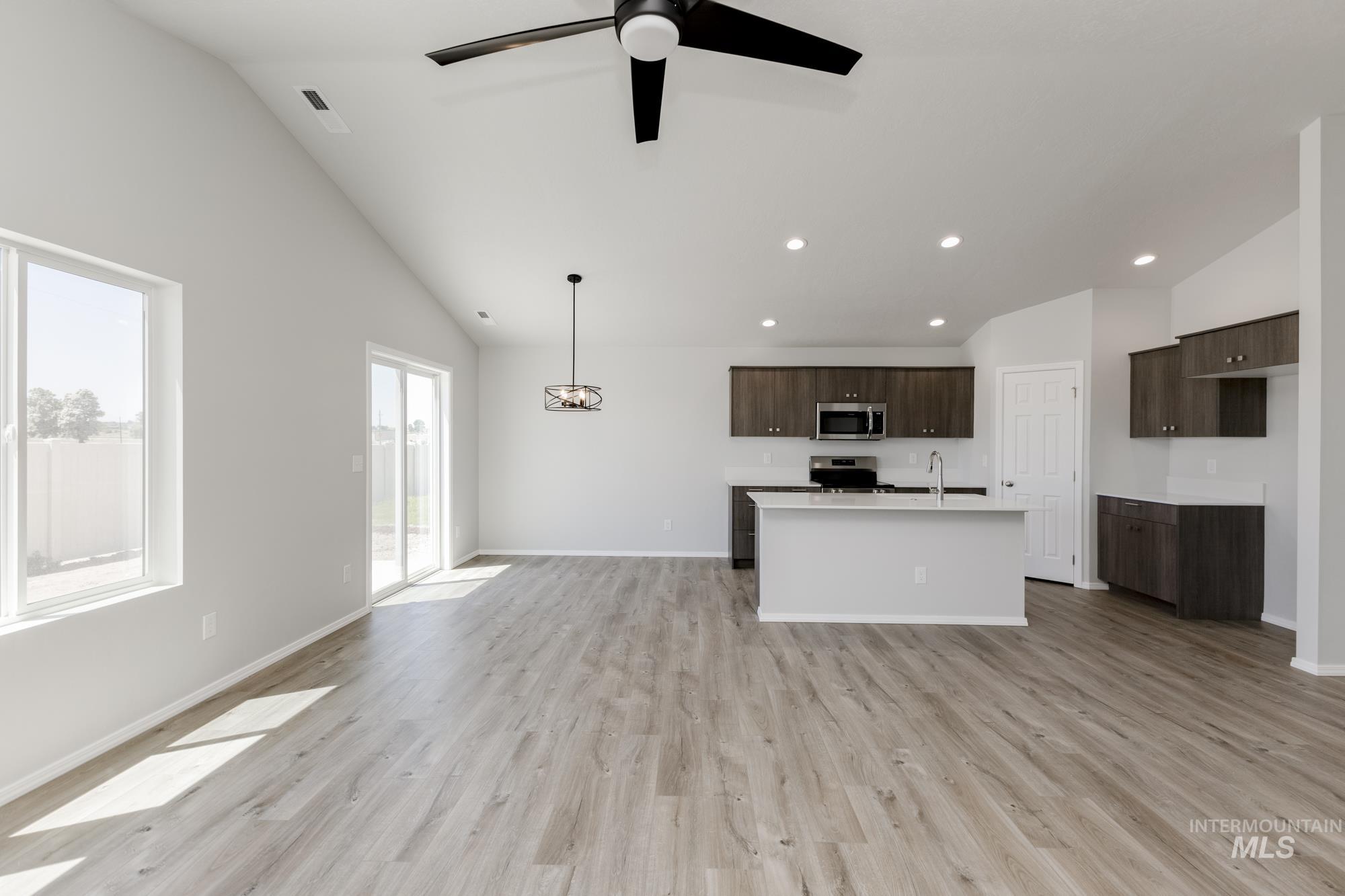 Kitchen with dark brown cabinets, open floor plan, light wood finished floors, an island with sink, and recessed lighting