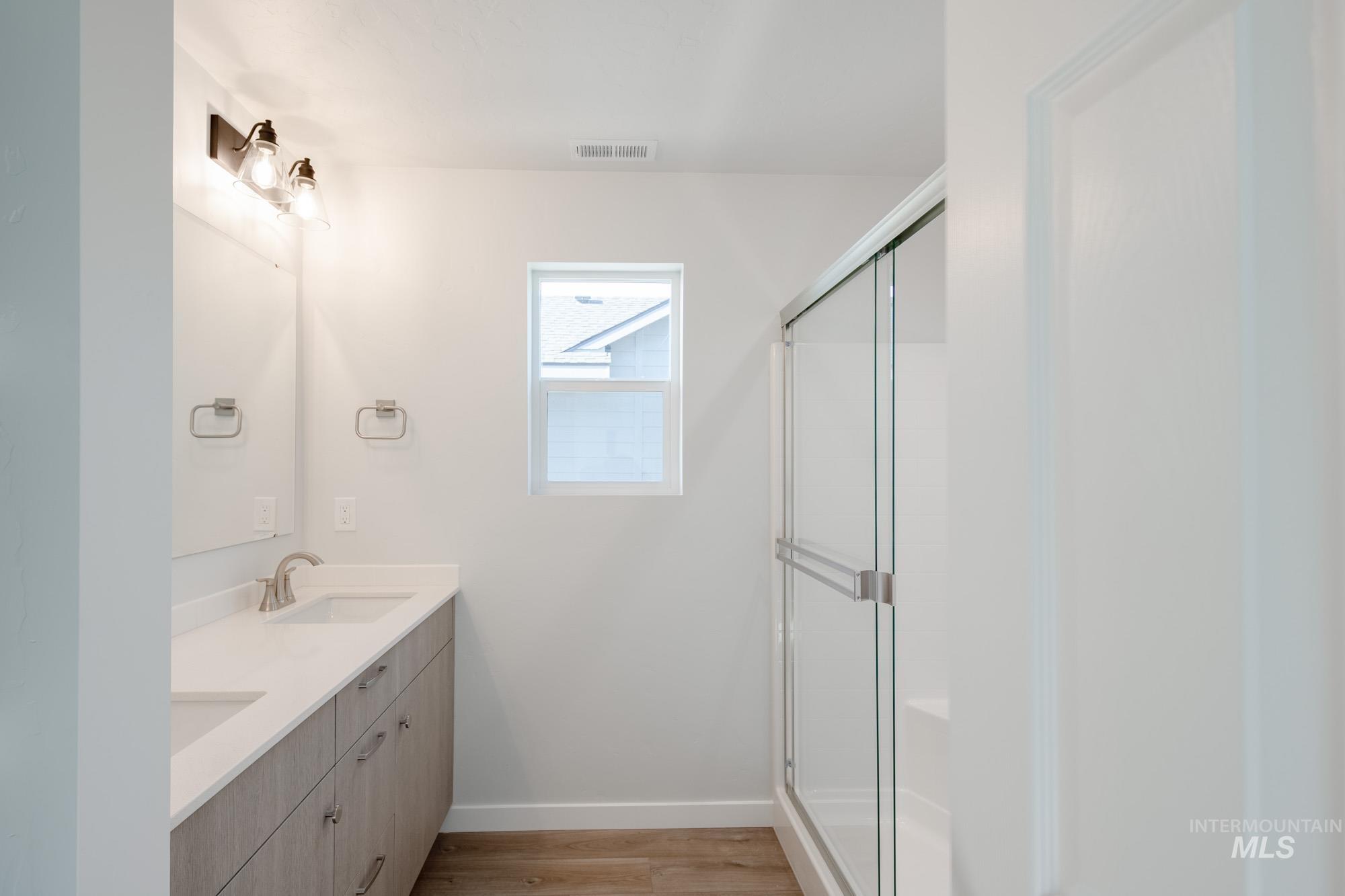 Full bath with double vanity, a shower stall, and light wood-style flooring