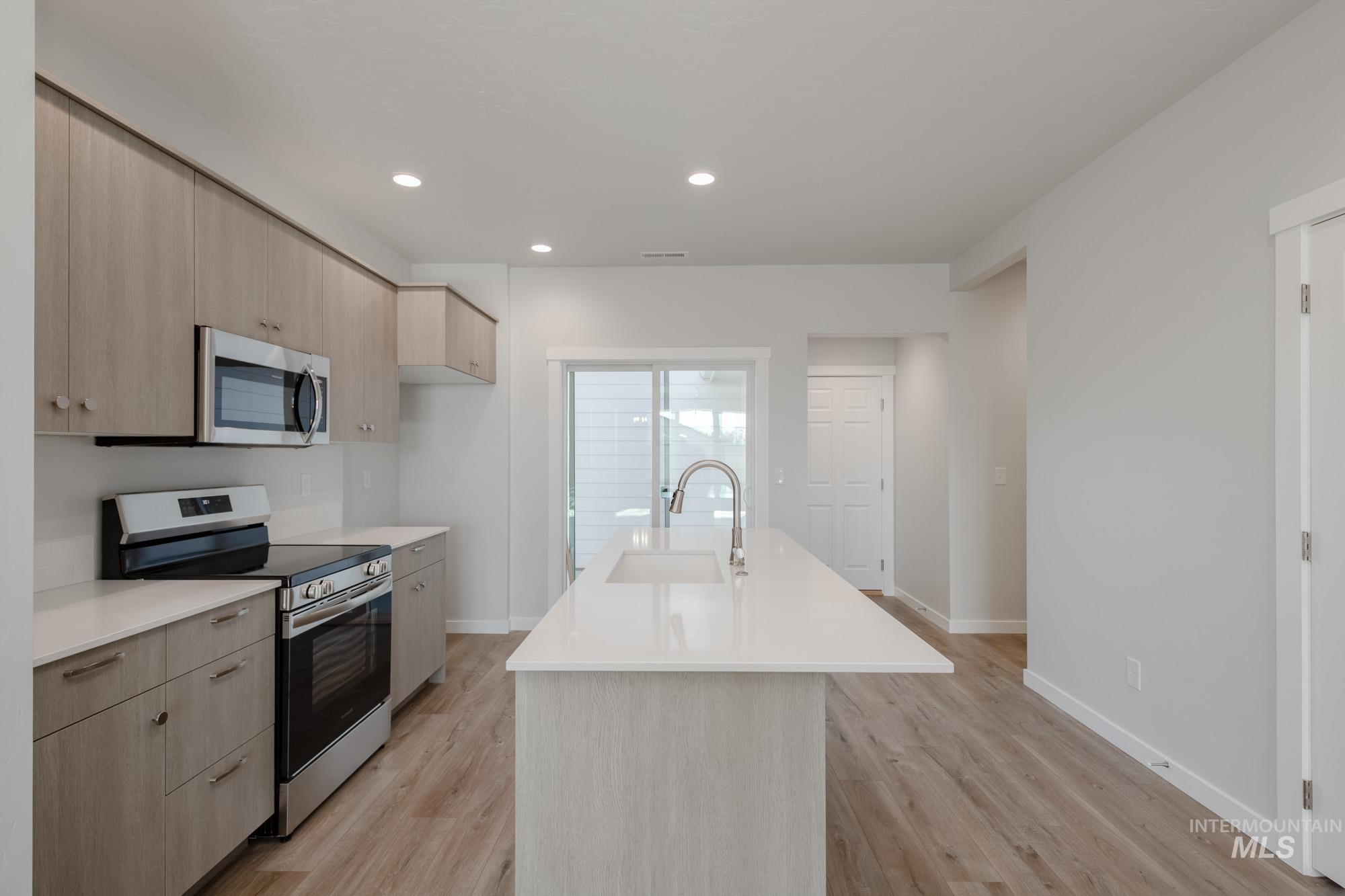 Kitchen with appliances with stainless steel finishes, light brown cabinetry, modern cabinets, recessed lighting, and an island with sink