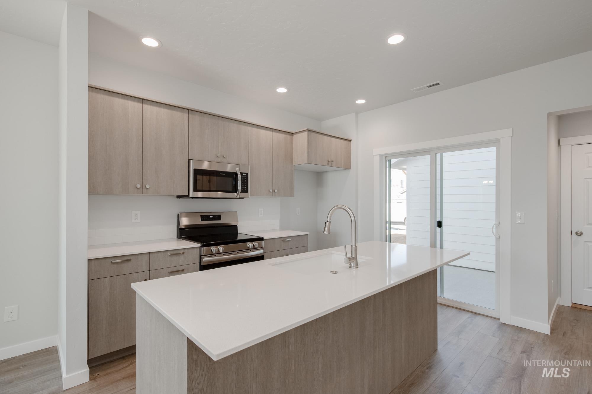 Kitchen with light brown cabinets, modern cabinets, stainless steel appliances, light stone countertops, and recessed lighting