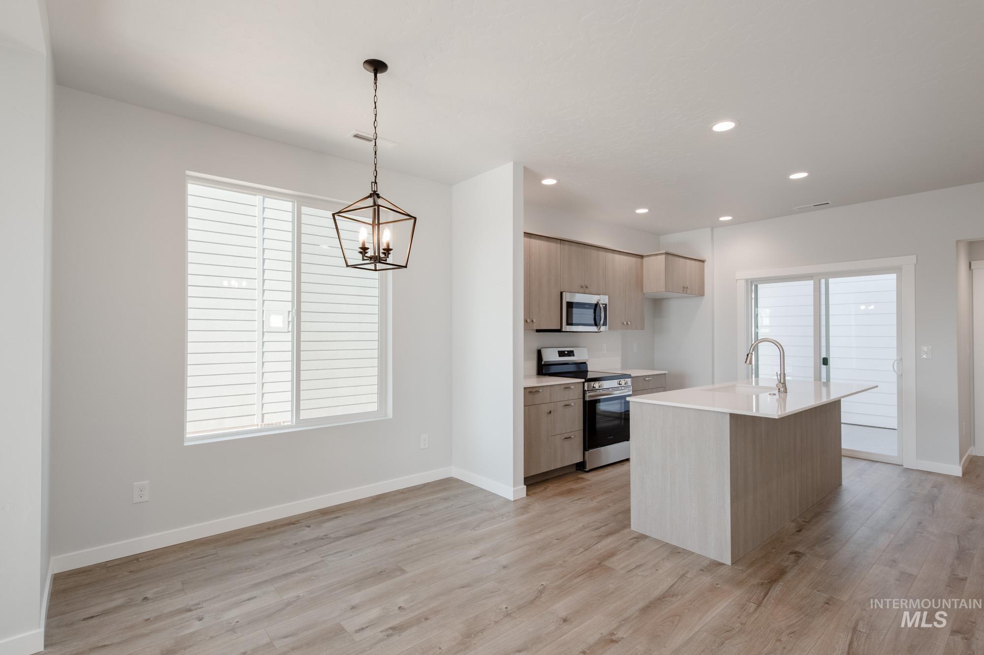 Kitchen with stainless steel appliances, an island with sink, modern cabinets, hanging light fixtures, and light wood finished floors