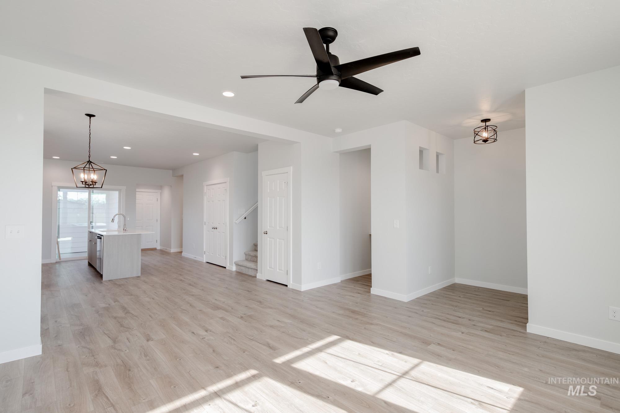 Unfurnished living room with a chandelier, light wood-style flooring, recessed lighting, a ceiling fan, and stairway