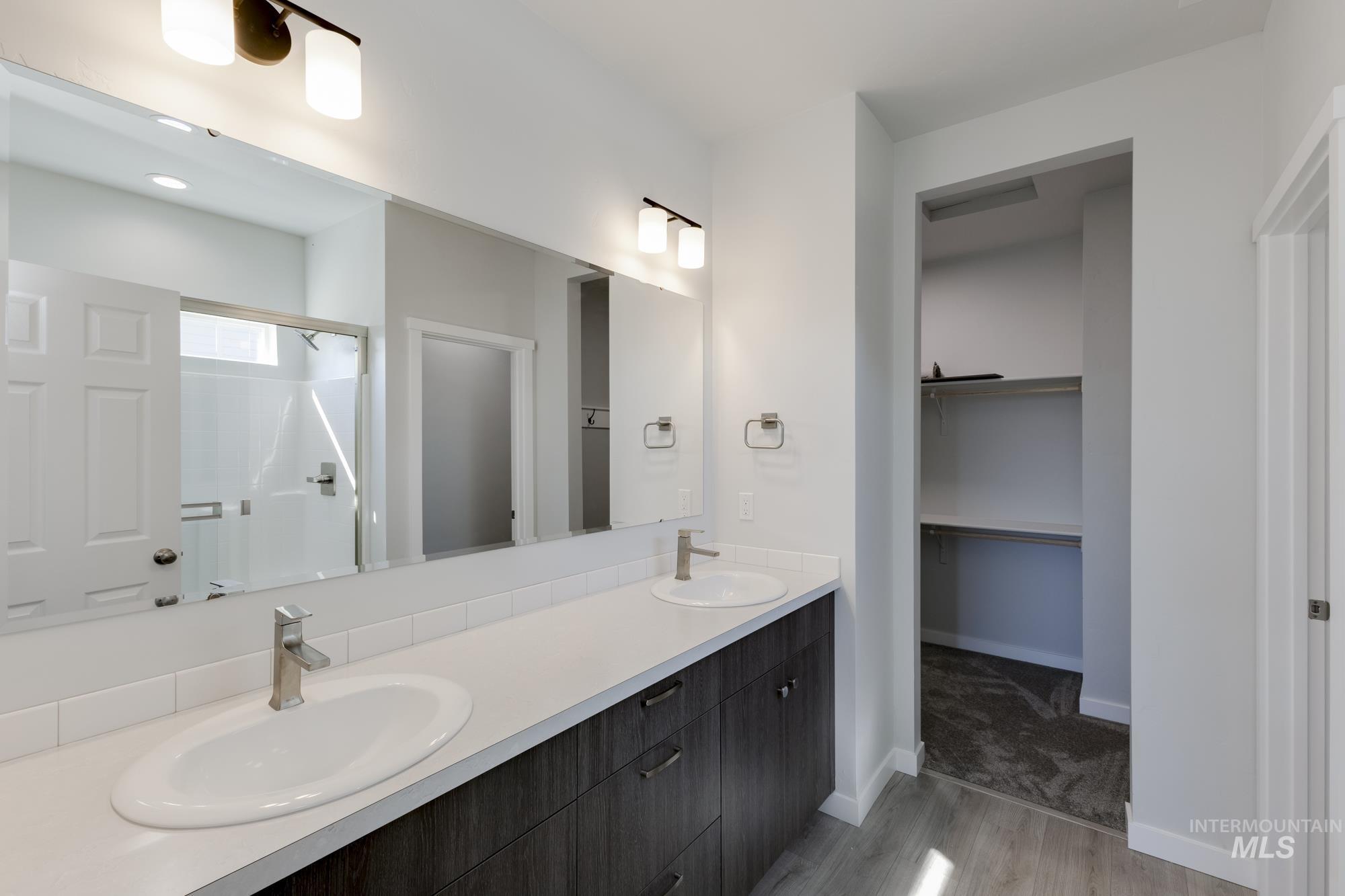 Bathroom with light wood-type flooring, double vanity, a shower stall, and a walk in closet