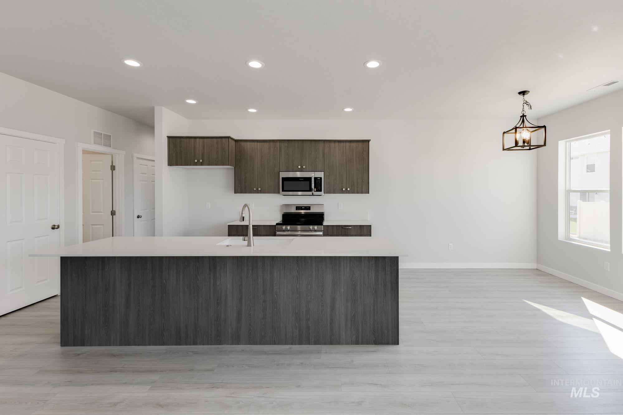 Kitchen with dark brown cabinets, appliances with stainless steel finishes, recessed lighting, light wood-style floors, and a center island with sink
