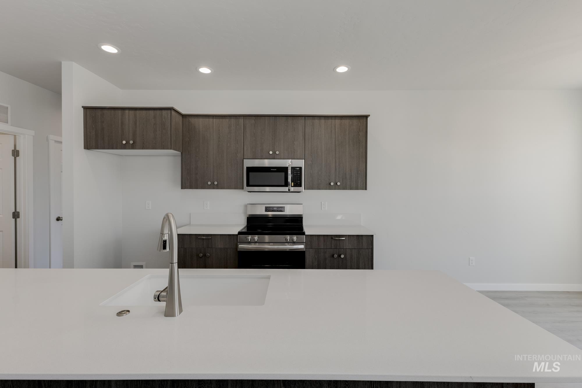 Kitchen featuring dark brown cabinetry, appliances with stainless steel finishes, modern cabinets, recessed lighting, and light stone countertops