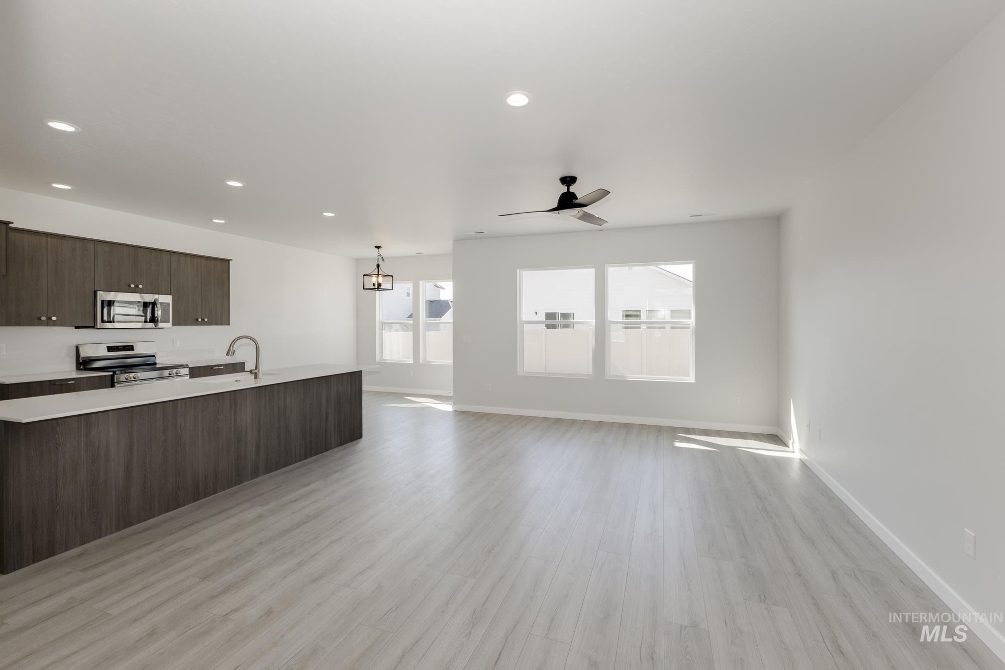 Kitchen with dark brown cabinetry, open floor plan, appliances with stainless steel finishes, light wood-style flooring, and pendant lighting