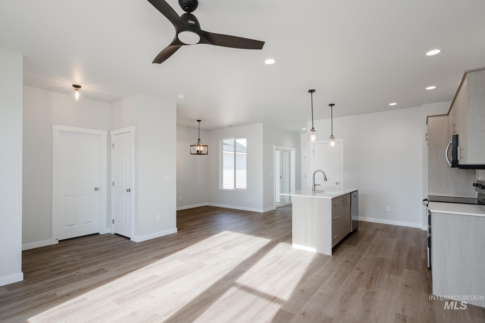 Kitchen featuring stainless steel appliances, an island with sink, light wood-type flooring, open floor plan, and hanging light fixtures