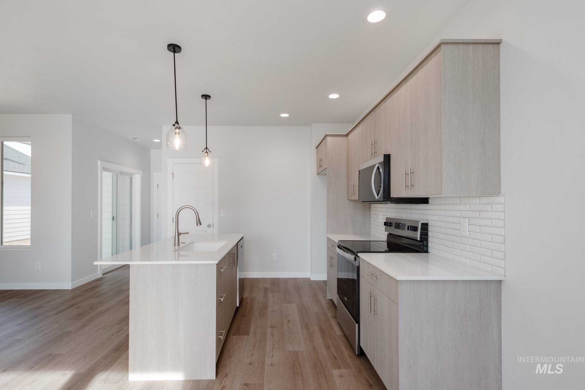 Kitchen featuring light brown cabinetry, stainless steel appliances, modern cabinets, a kitchen island with sink, and recessed lighting