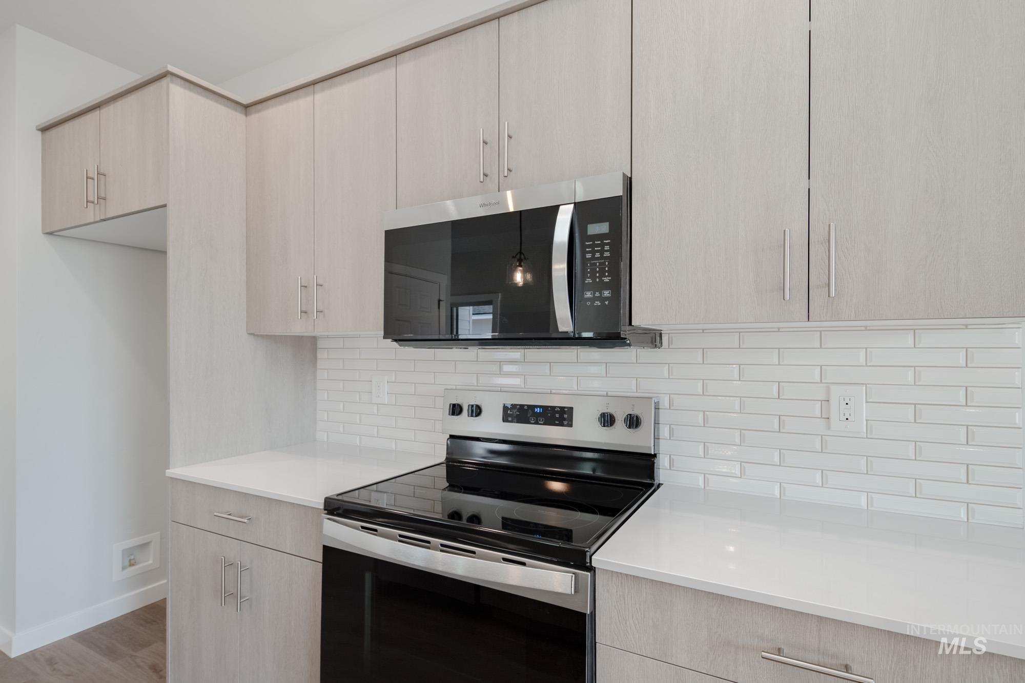 Kitchen featuring light brown cabinetry, stainless steel appliances, modern cabinets, backsplash, and light wood-style floors
