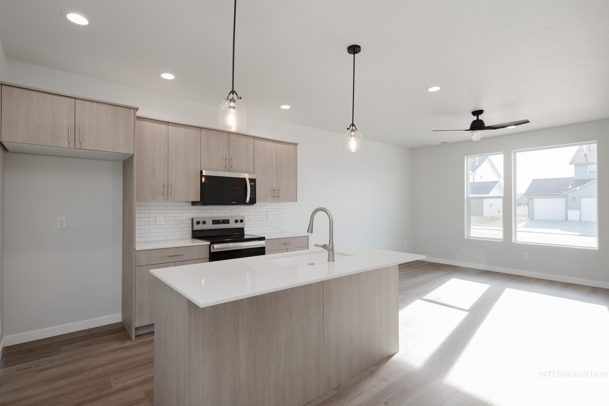Kitchen featuring light brown cabinets, tasteful backsplash, pendant lighting, appliances with stainless steel finishes, and a kitchen island with sink