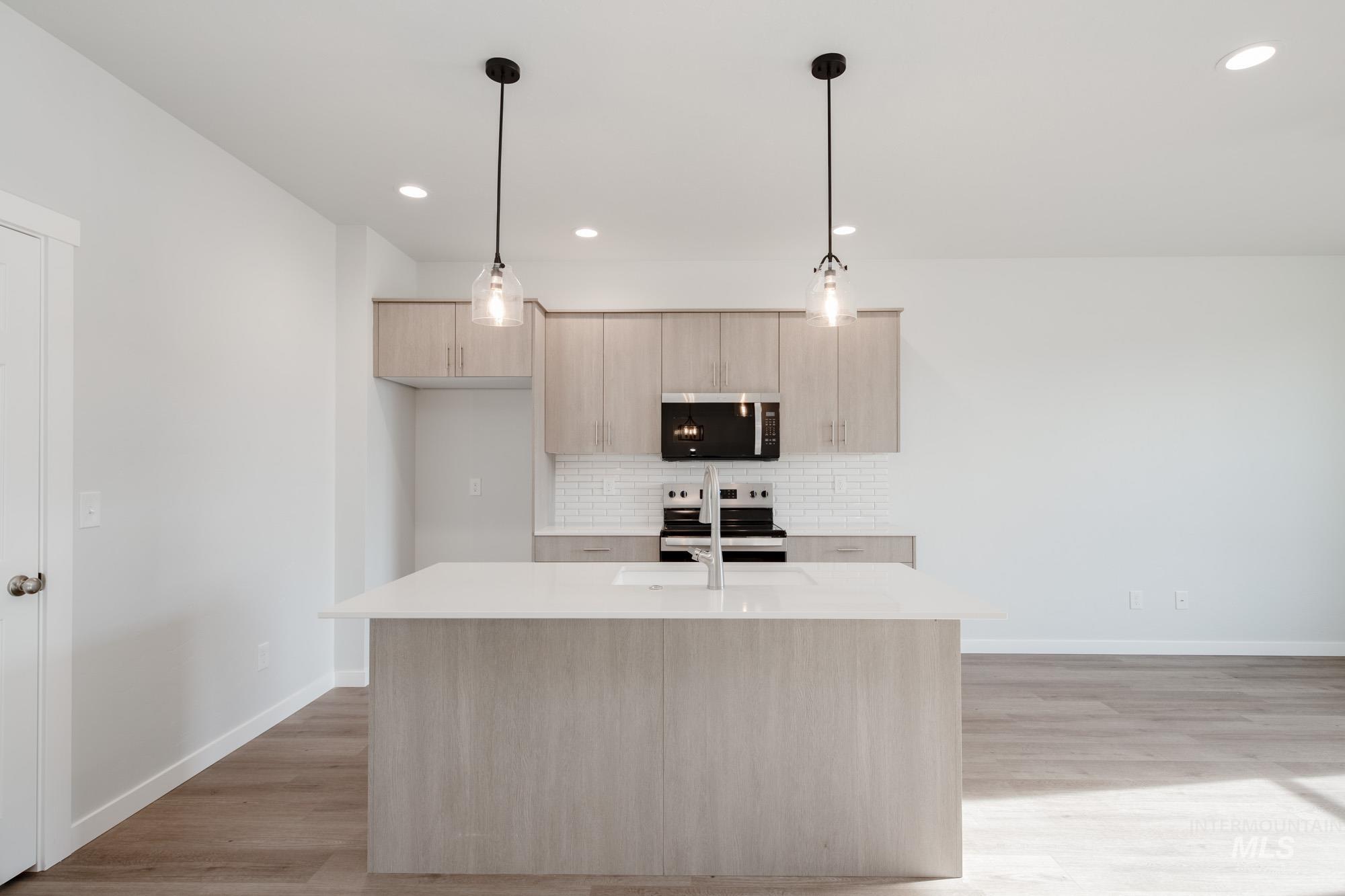 Kitchen featuring light brown cabinetry, decorative backsplash, stainless steel appliances, hanging light fixtures, and light stone counters