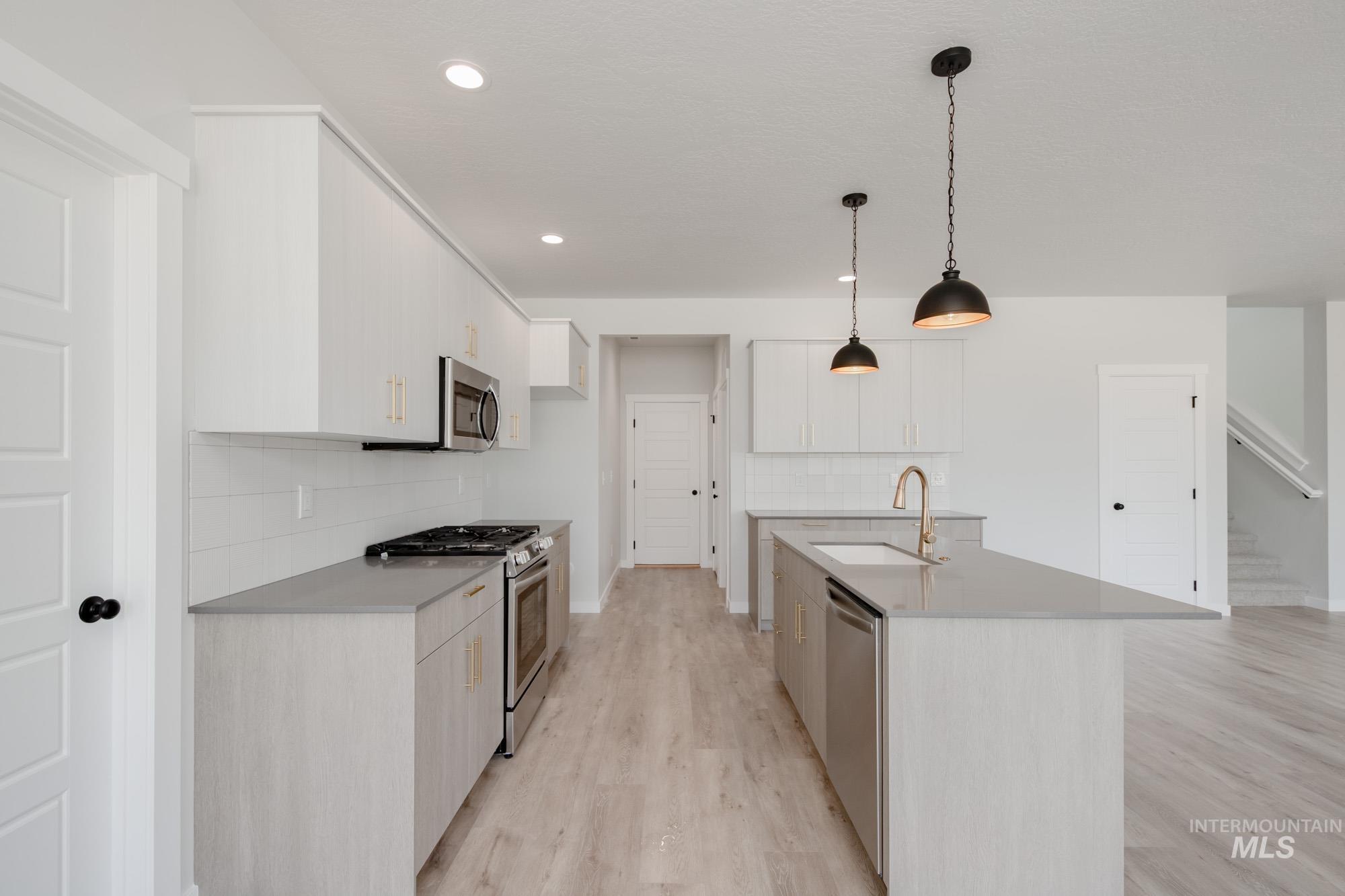 Kitchen featuring appliances with stainless steel finishes, backsplash, light wood-style floors, hanging light fixtures, and a center island with sink