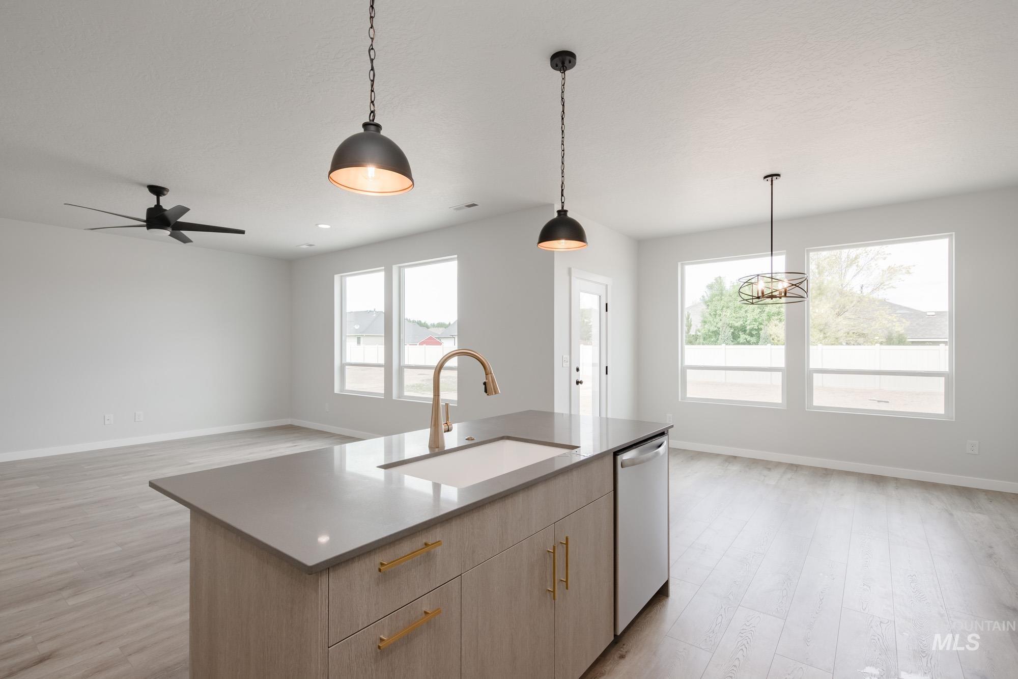 Kitchen with light wood-style floors, light brown cabinetry, decorative light fixtures, open floor plan, and a center island with sink
