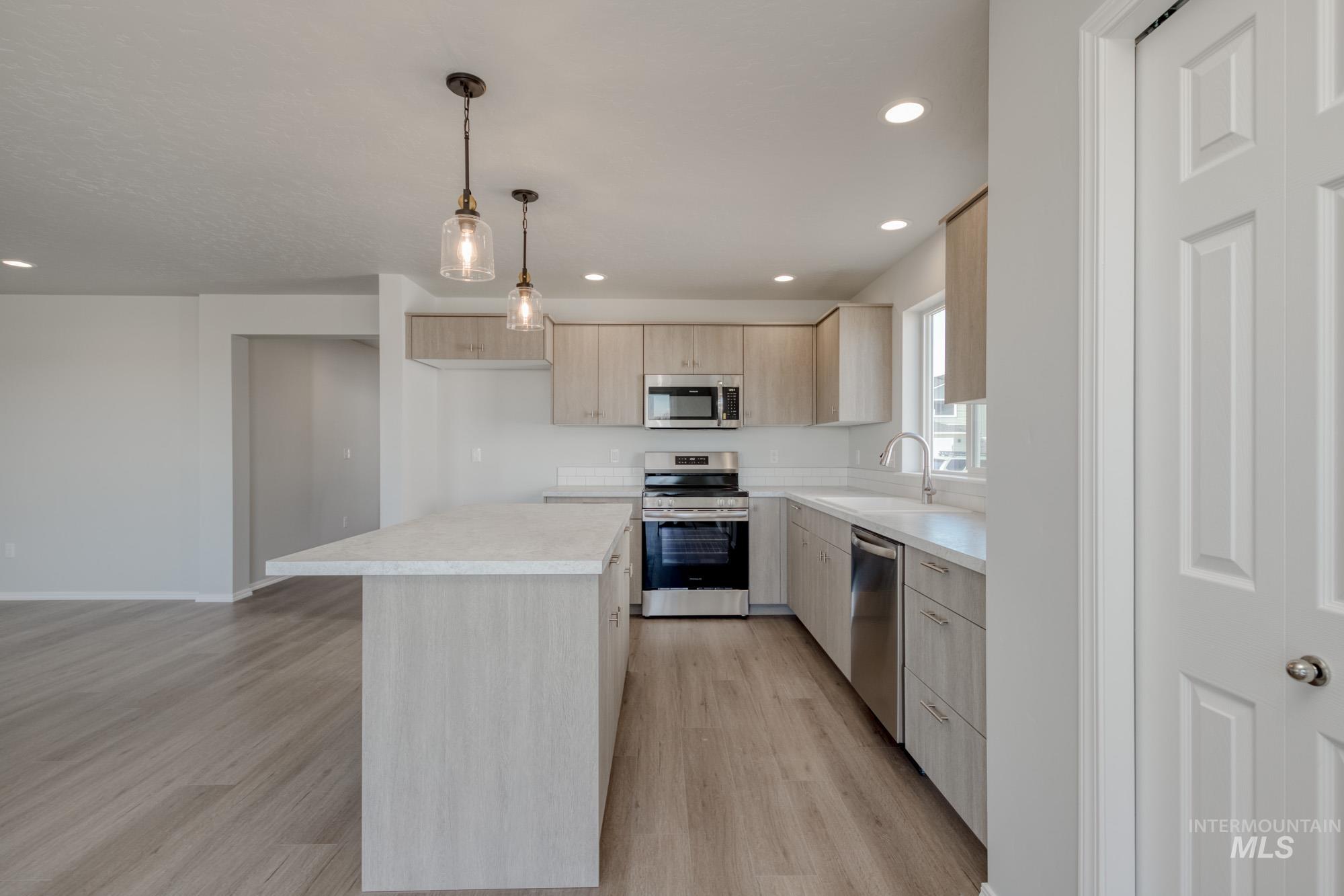 Kitchen featuring stainless steel appliances, light countertops, light brown cabinetry, recessed lighting, and light wood-type flooring