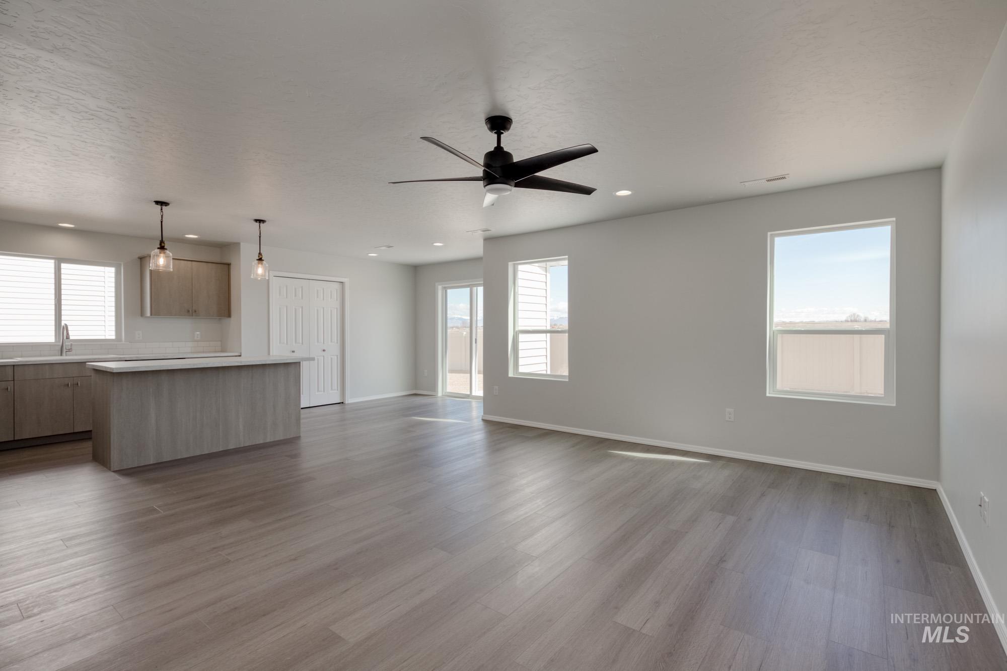 Unfurnished living room with plenty of natural light, dark wood finished floors, a ceiling fan, a textured ceiling, and recessed lighting