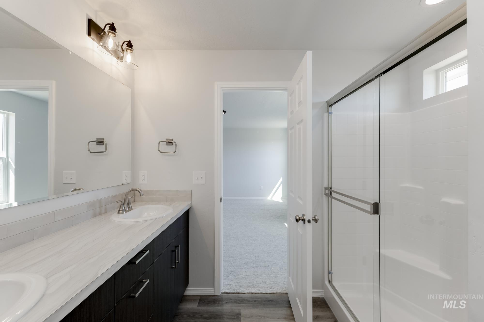 Full bathroom featuring double vanity, dark wood finished floors, and a stall shower