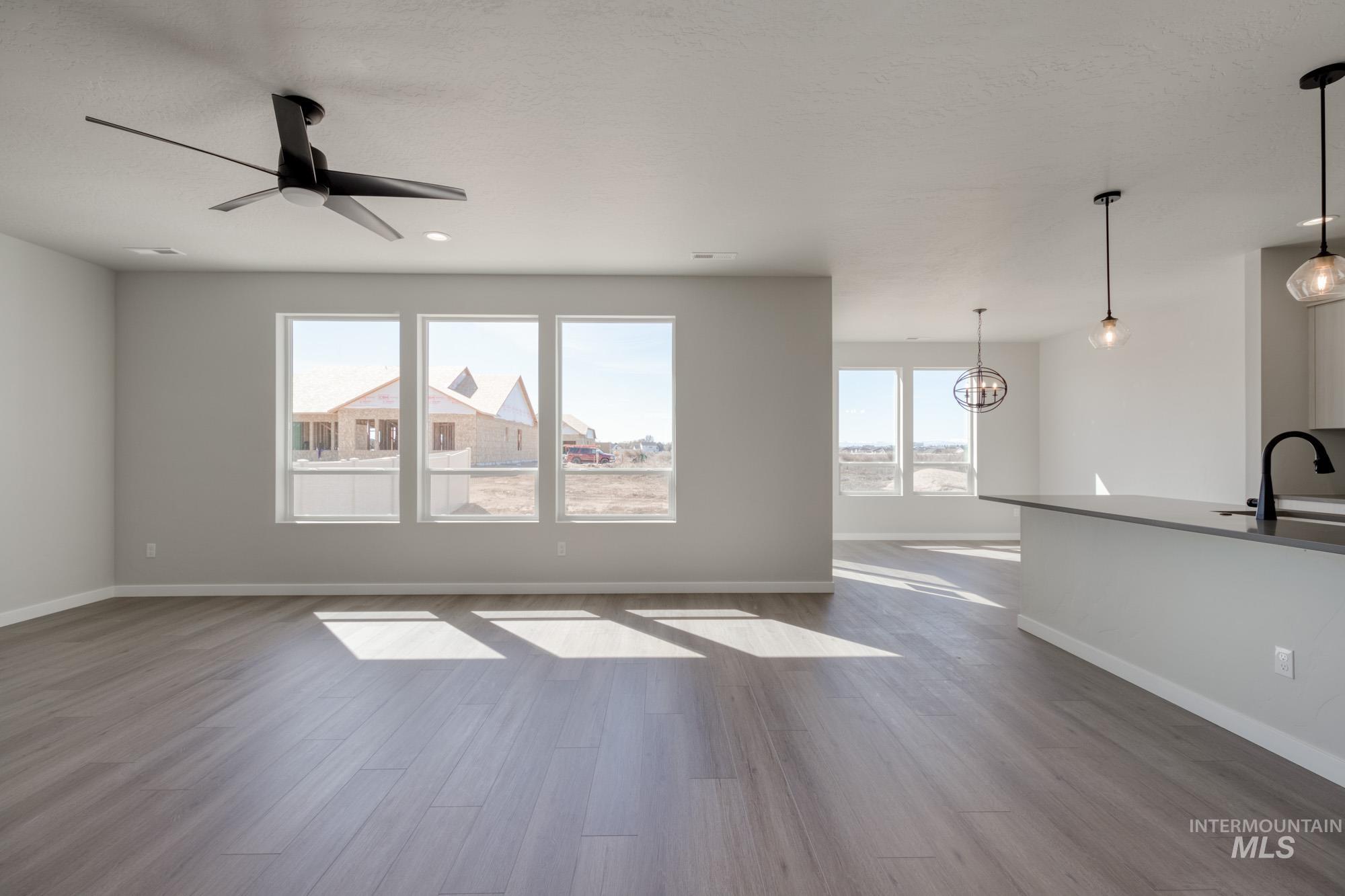 Unfurnished living room featuring dark wood-style floors, plenty of natural light, and a ceiling fan