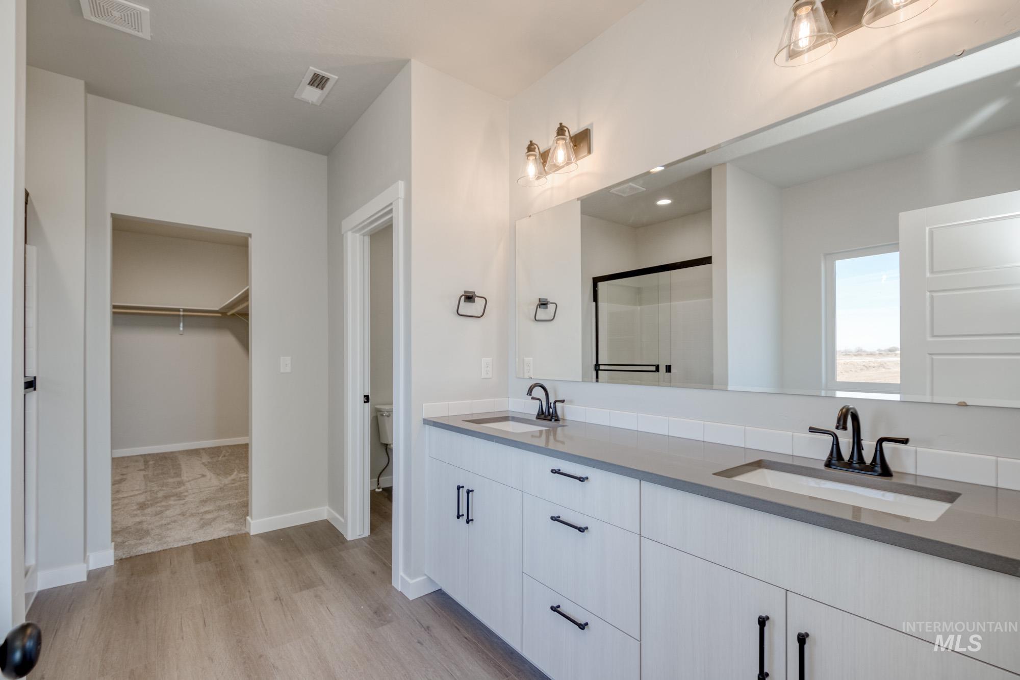 Full bath featuring a stall shower, light wood-type flooring, double vanity, and a walk in closet