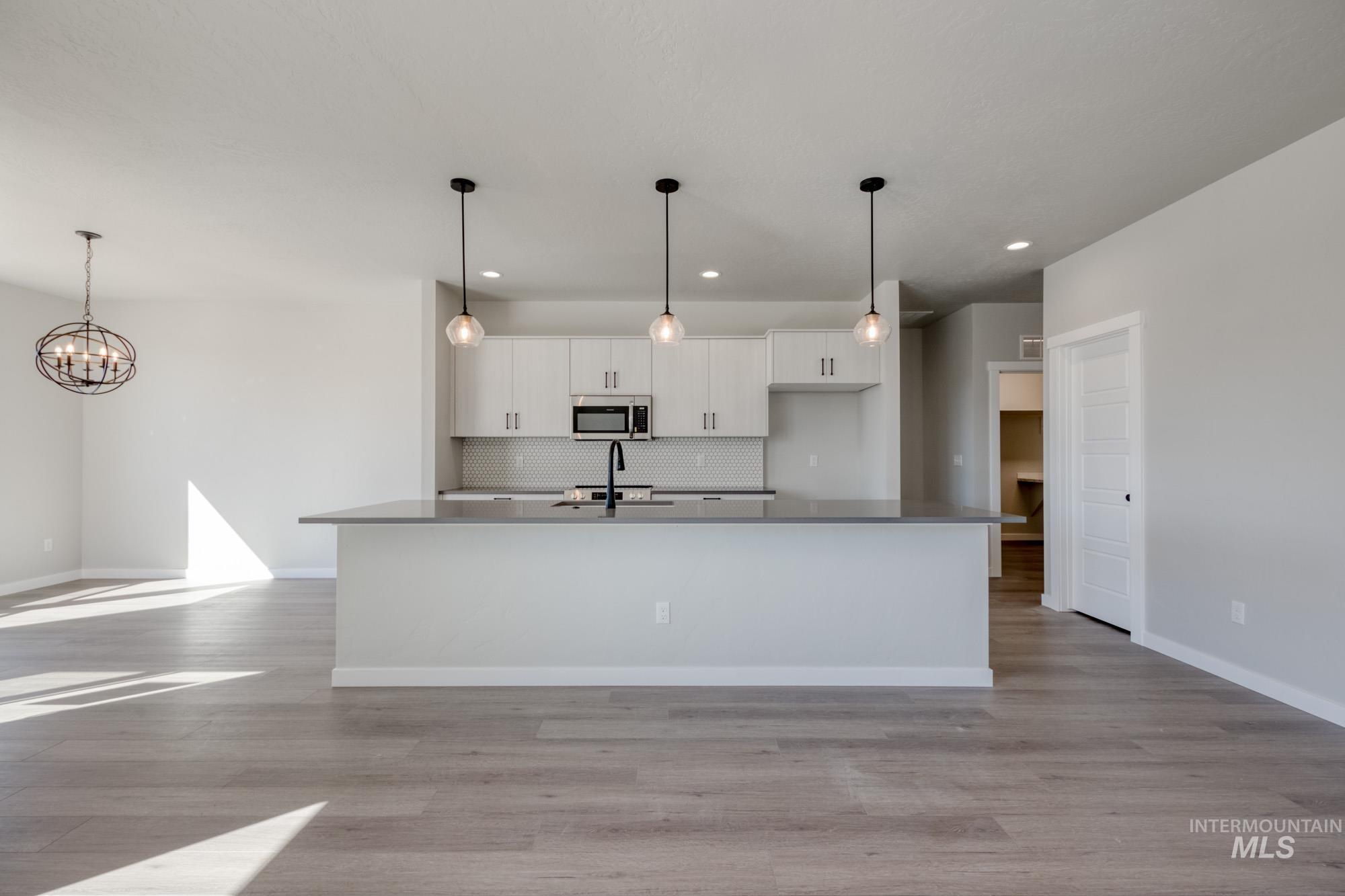 Kitchen with open floor plan, white cabinetry, pendant lighting, backsplash, and light wood-style floors