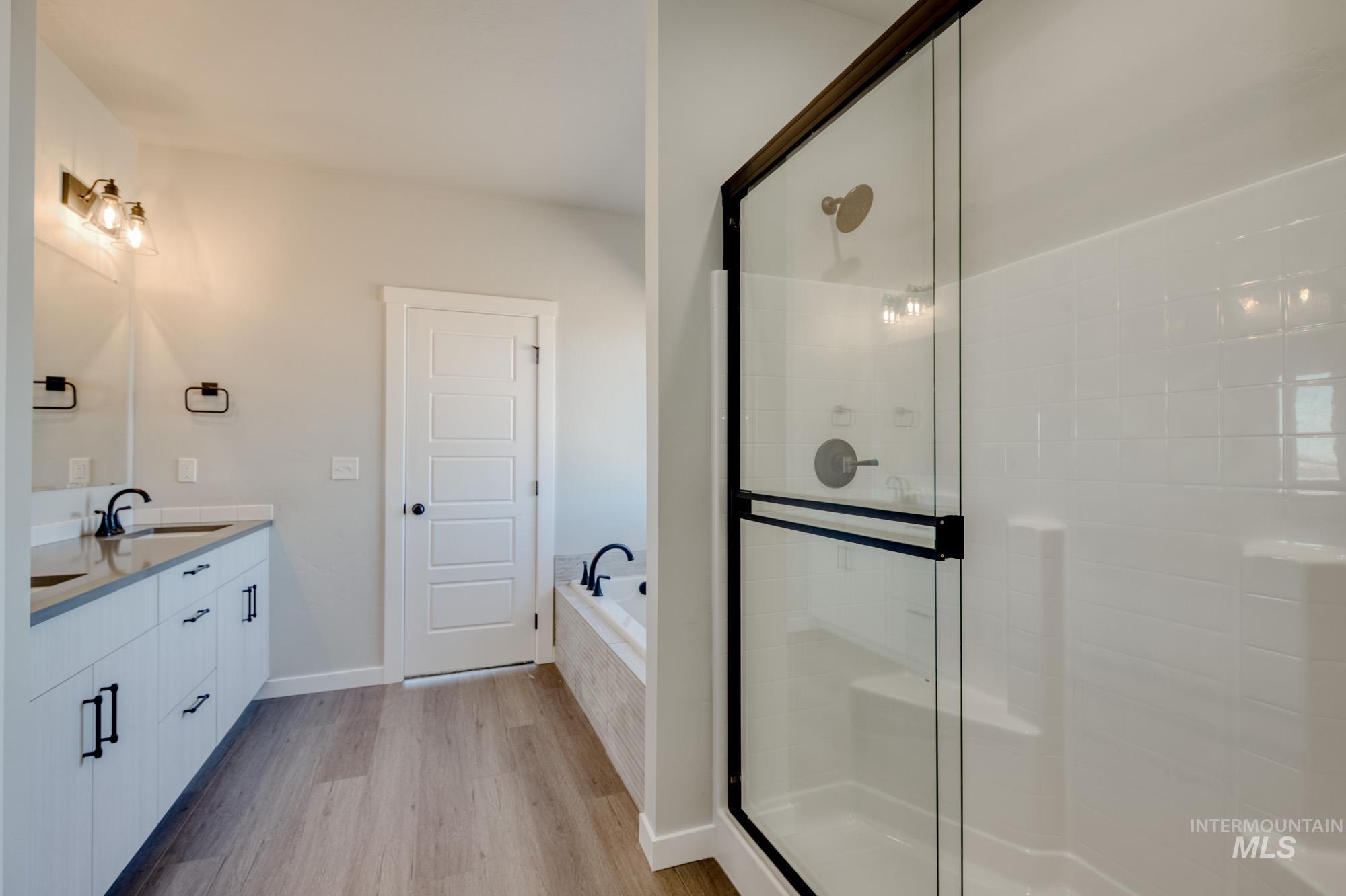 Bathroom with light wood-style floors, double vanity, a garden tub, and a shower stall
