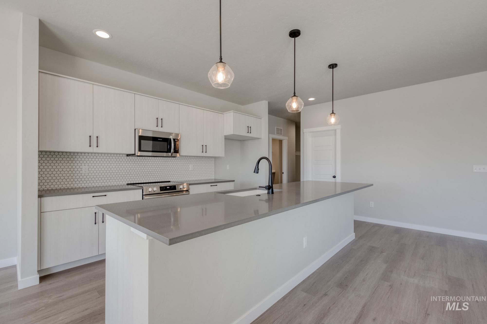 Kitchen featuring appliances with stainless steel finishes, light wood-type flooring, hanging light fixtures, decorative backsplash, and a center island with sink
