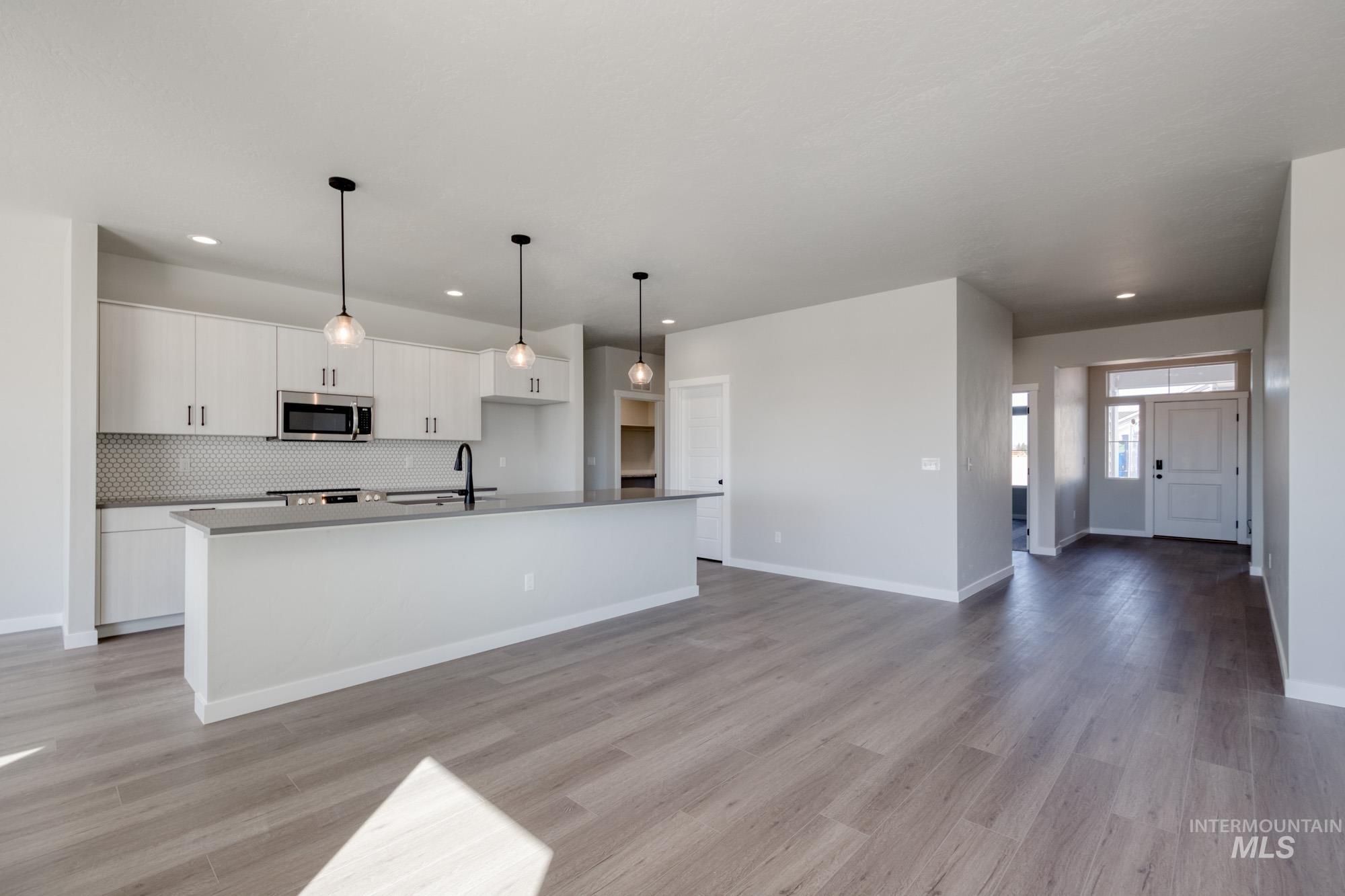 Kitchen with tasteful backsplash, open floor plan, white cabinetry, stainless steel microwave, and a kitchen island with sink