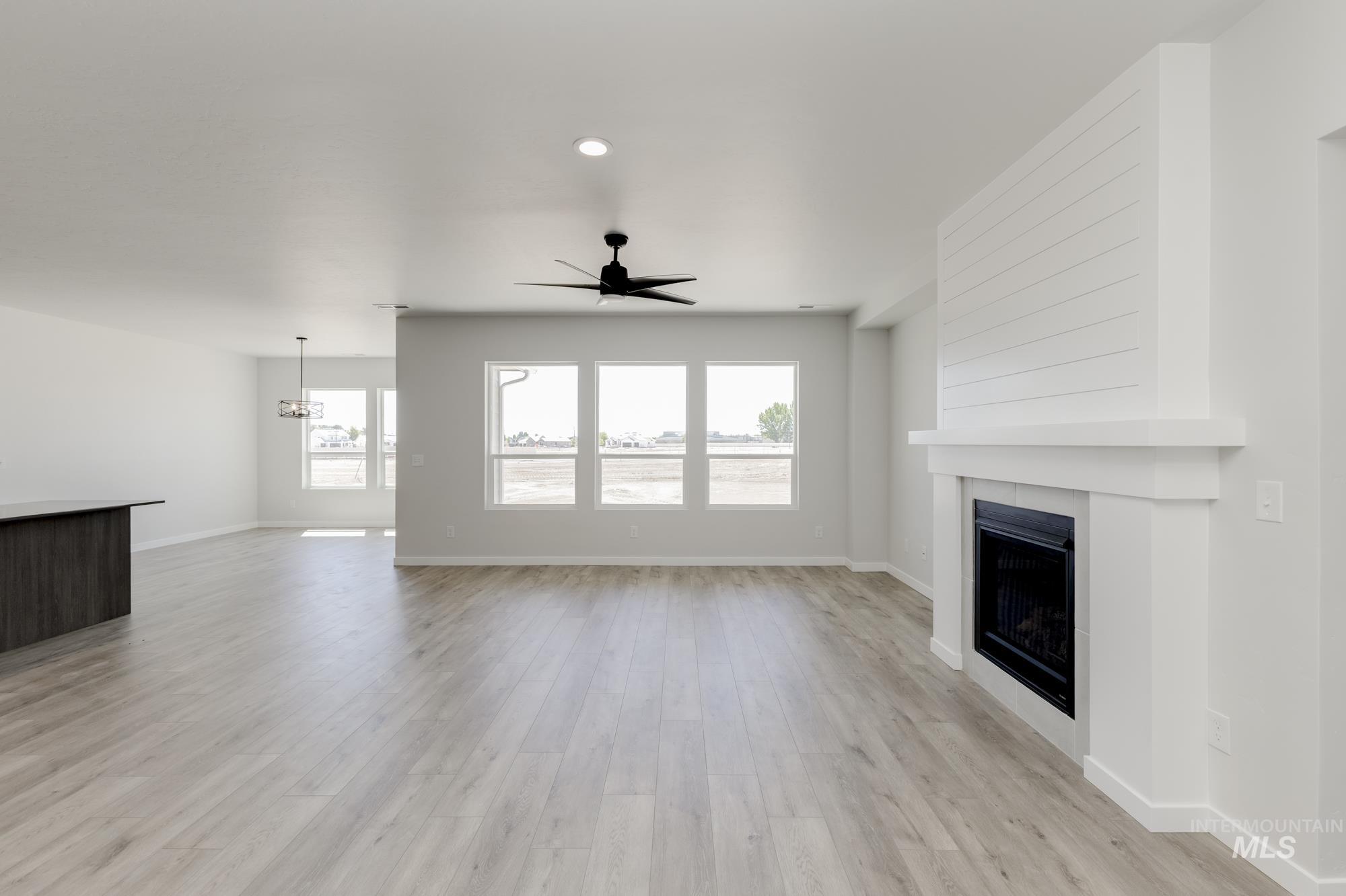 Unfurnished living room featuring ceiling fan, a fireplace, light wood finished floors, a chandelier, and recessed lighting