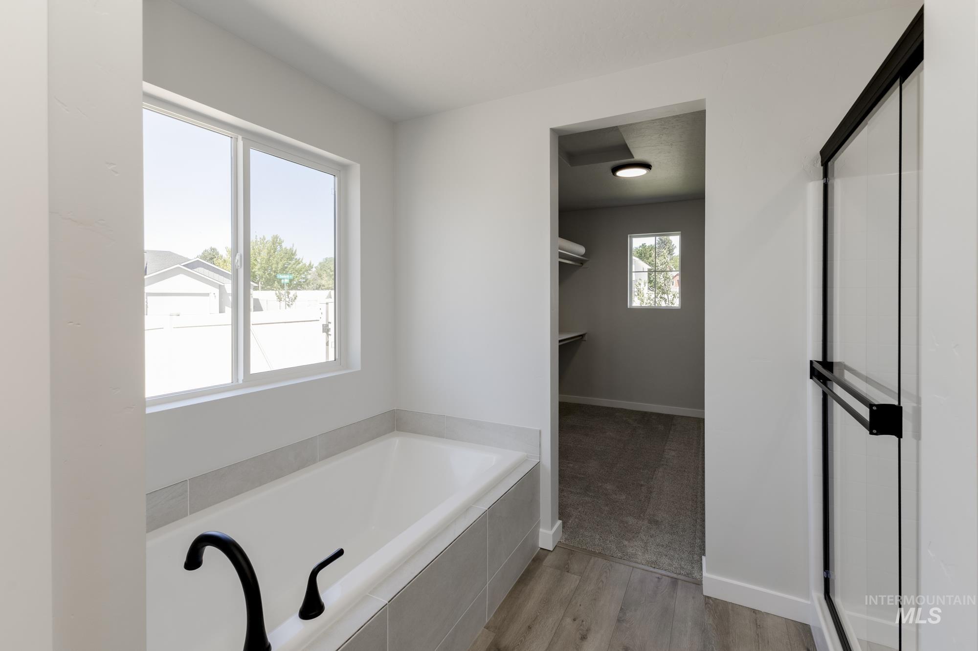 Full bathroom with light wood-type flooring, a walk in closet, a bath, and a stall shower
