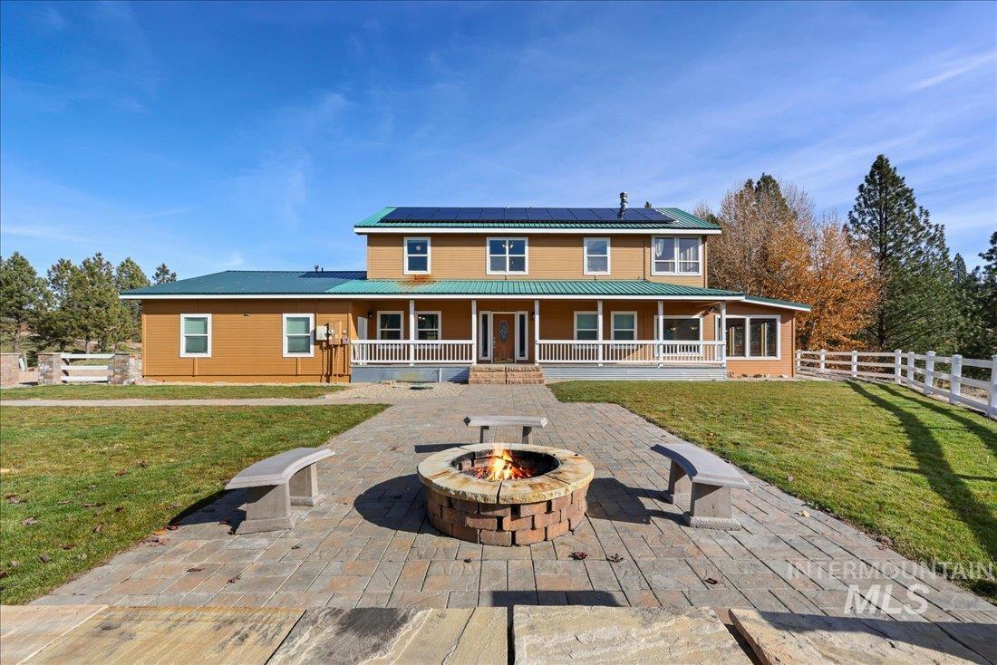 Rear view of property featuring a large porch, a fenced backyard, a metal roof, an outdoor fire pit, and roof mounted solar panels