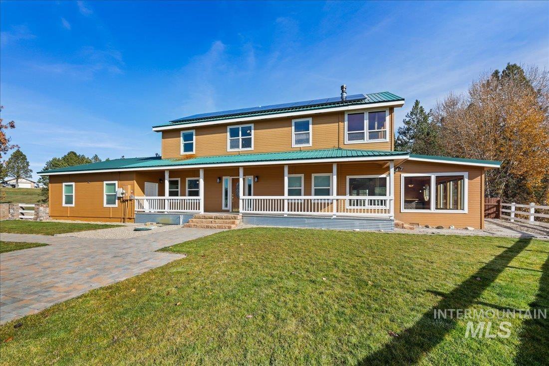 Rear view of property with a porch, roof mounted solar panels, and a lawn