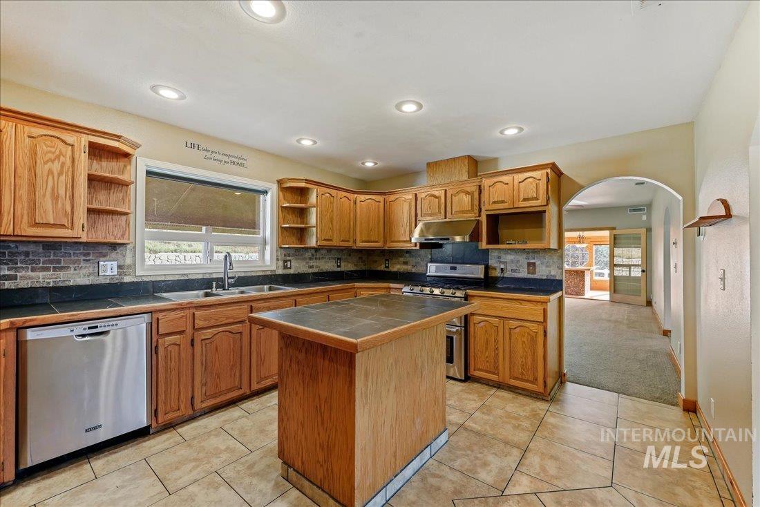 Kitchen with open shelves, arched walkways, decorative backsplash, appliances with stainless steel finishes, and recessed lighting