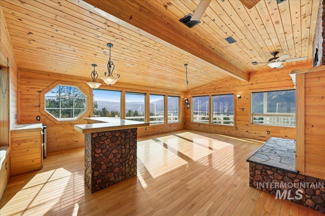 Unfurnished living room featuring wooden walls, light wood-style flooring, wooden ceiling, and a mountain view