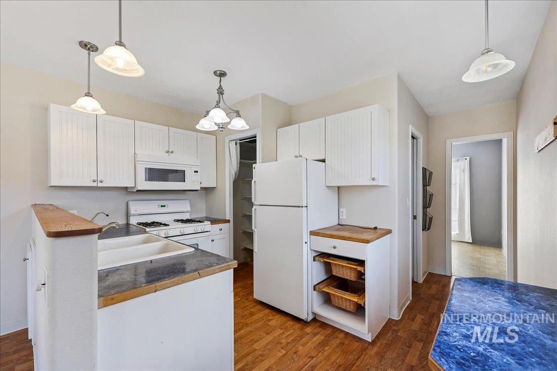 Kitchen featuring white cabinetry, white appliances, decorative light fixtures, dark wood-style flooring, and wood counters