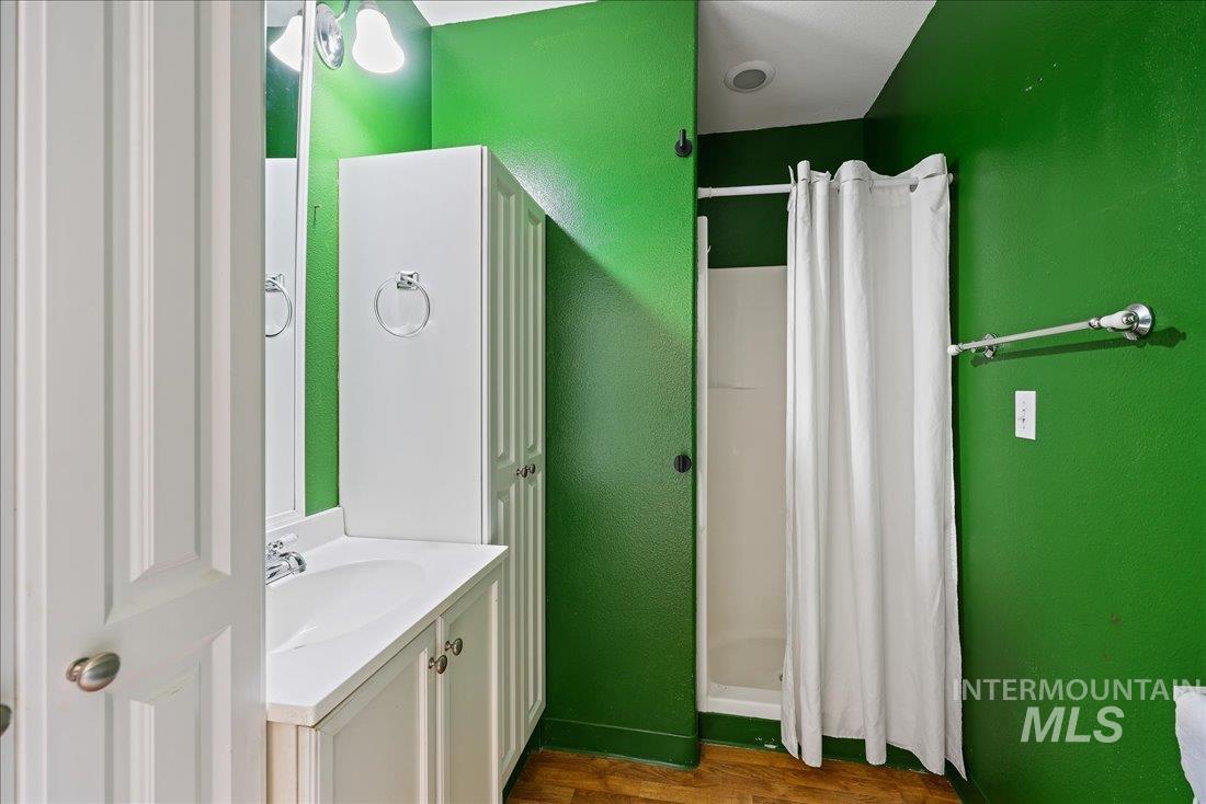 Full bathroom with a shower stall, vanity, dark wood finished floors, and a textured wall