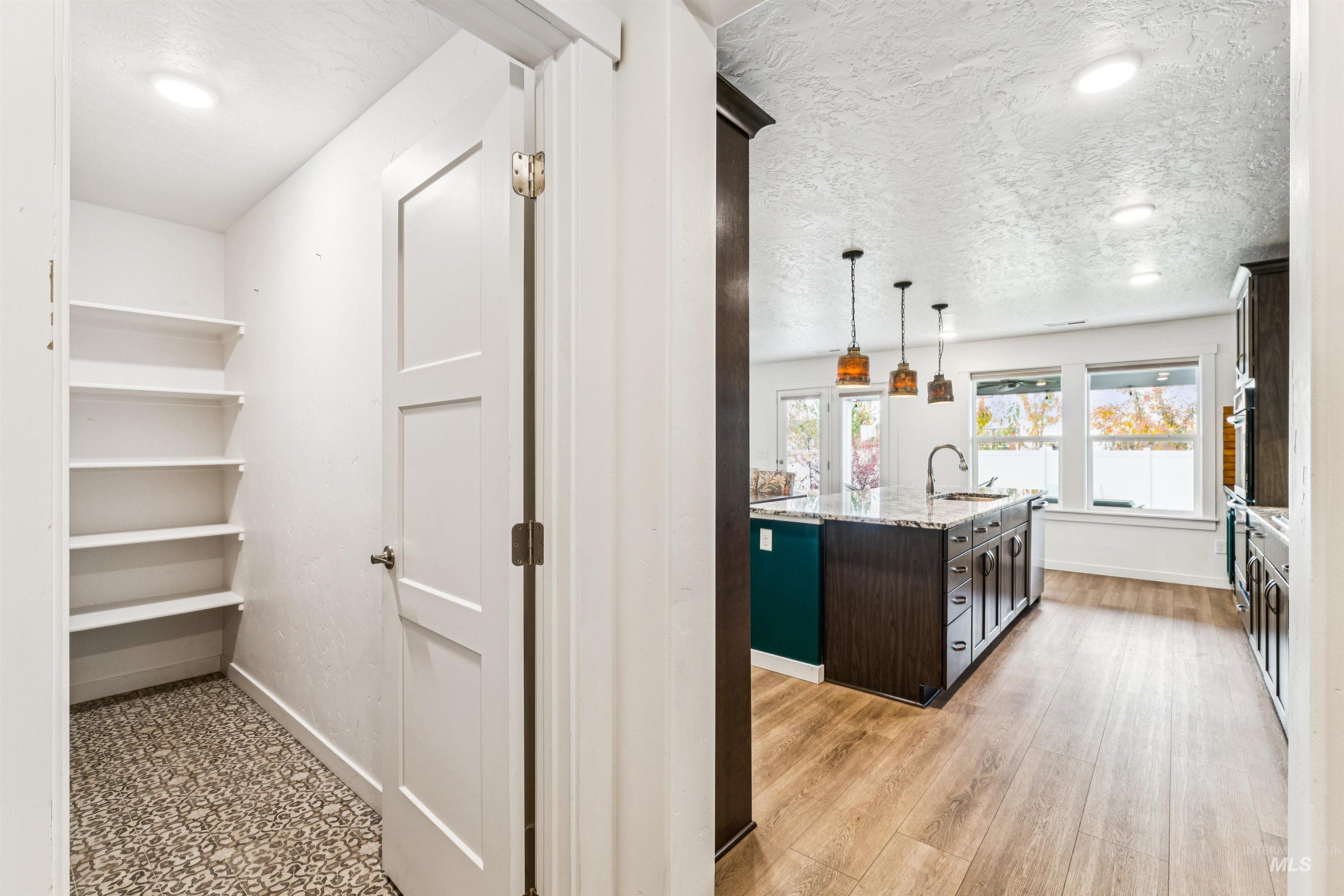 Kitchen featuring dark brown cabinets, a center island with sink, pendant lighting, light stone counters, and a textured ceiling
