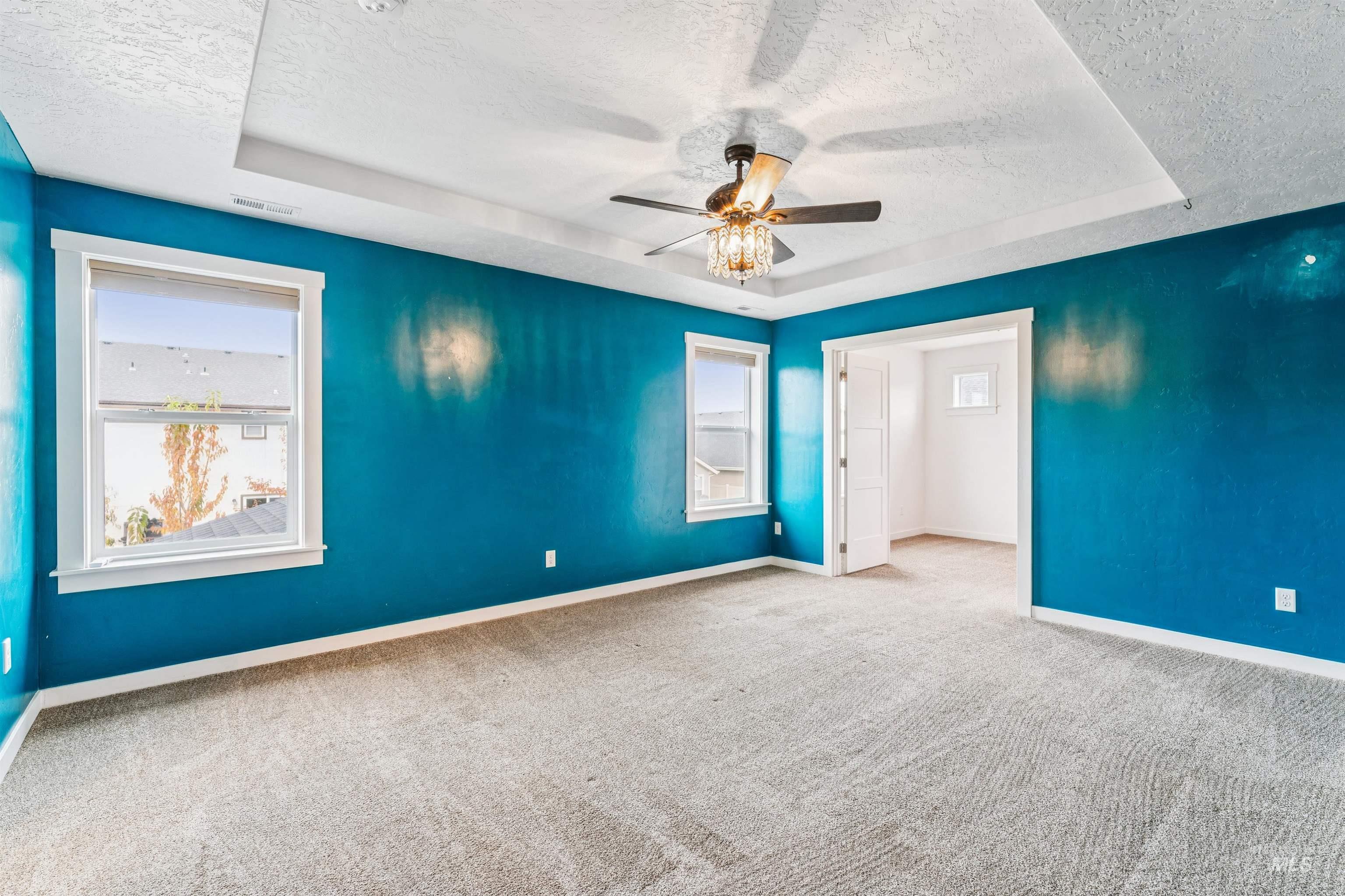 Empty room with a raised ceiling, a textured ceiling, carpet flooring, and a ceiling fan