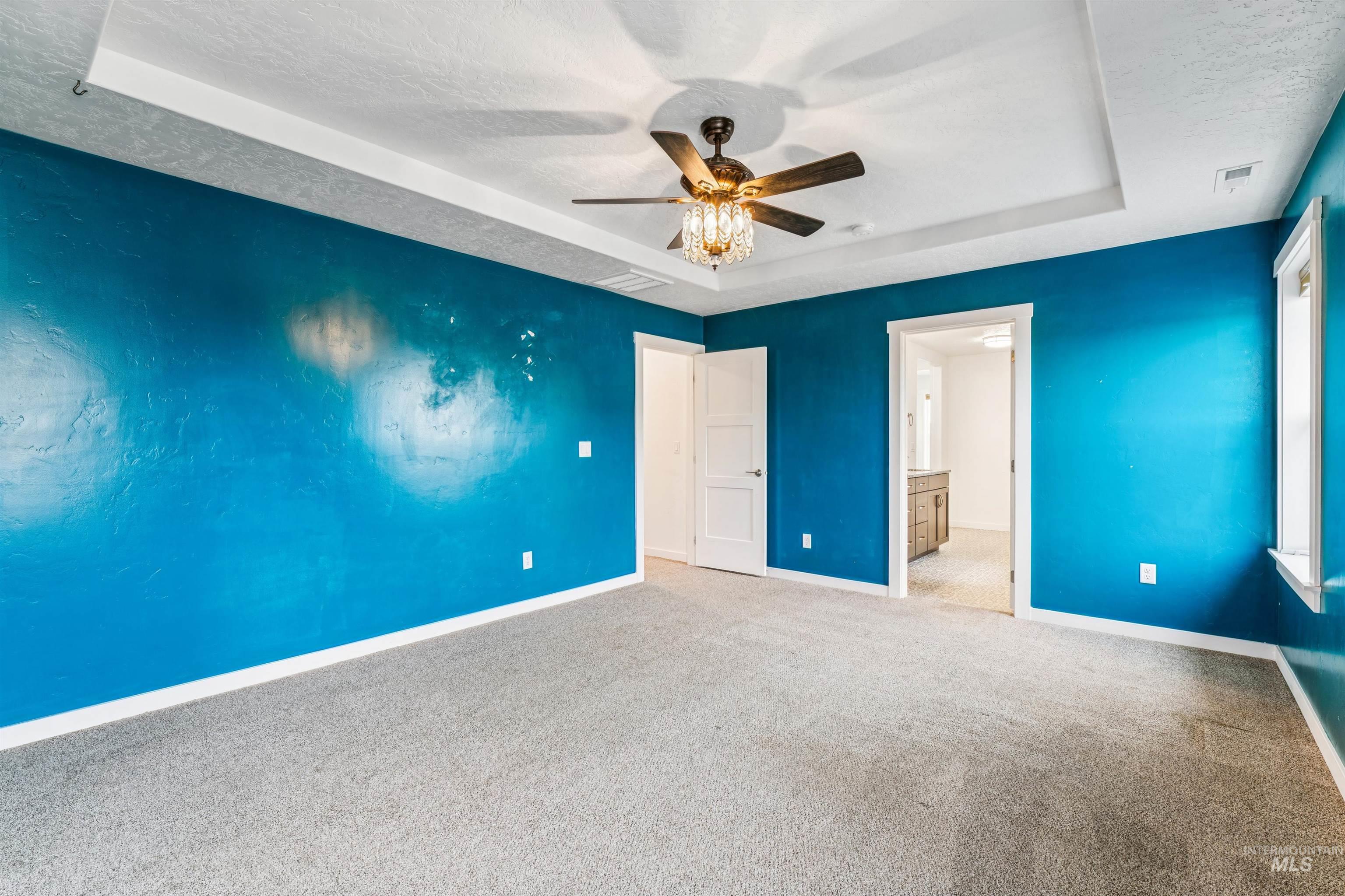 Unfurnished bedroom with a raised ceiling, carpet floors, a textured ceiling, a ceiling fan, and ensuite bath